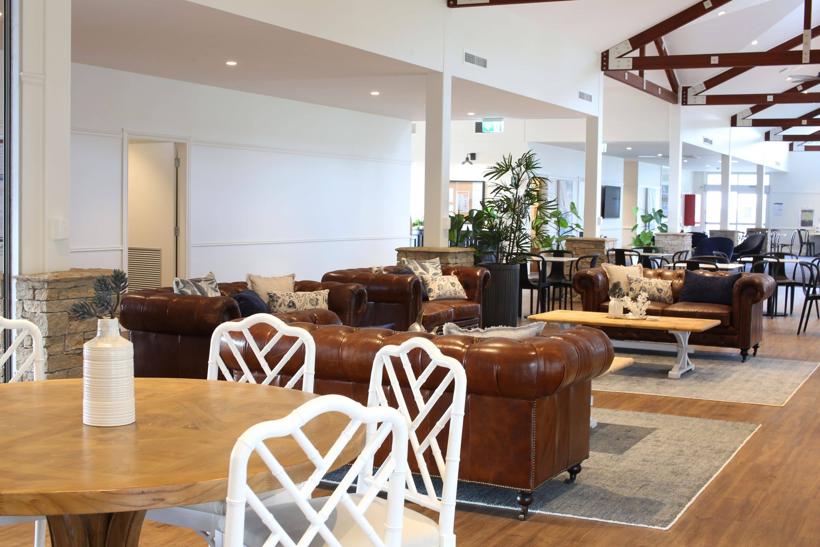 A spacious lounge area in an Ingenia Lifestyle community with leather sofas, wooden tables, and white chairs.