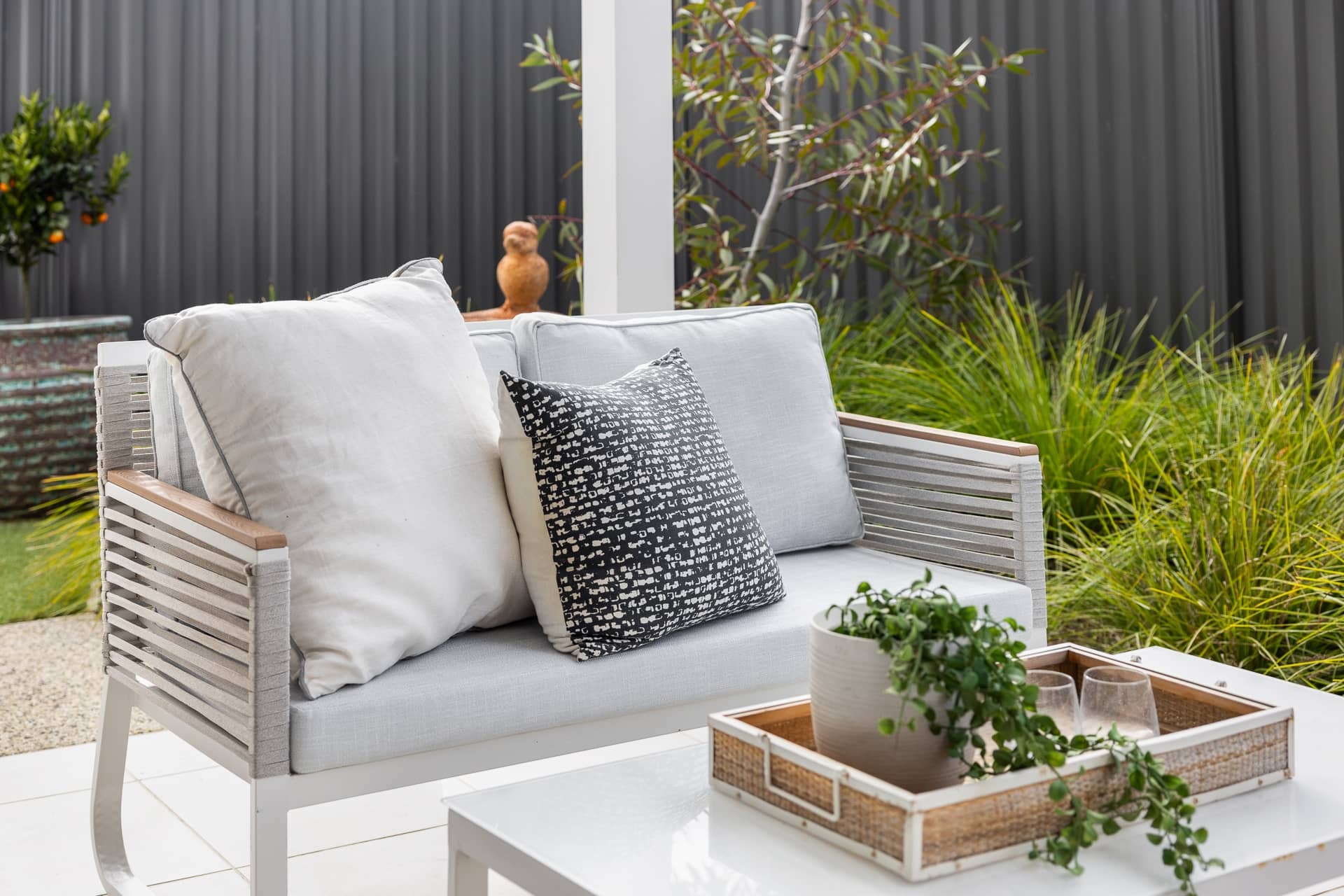 An outdoor lounge chair with grey cushions and white pillows sits on a patio next to a coffee table.