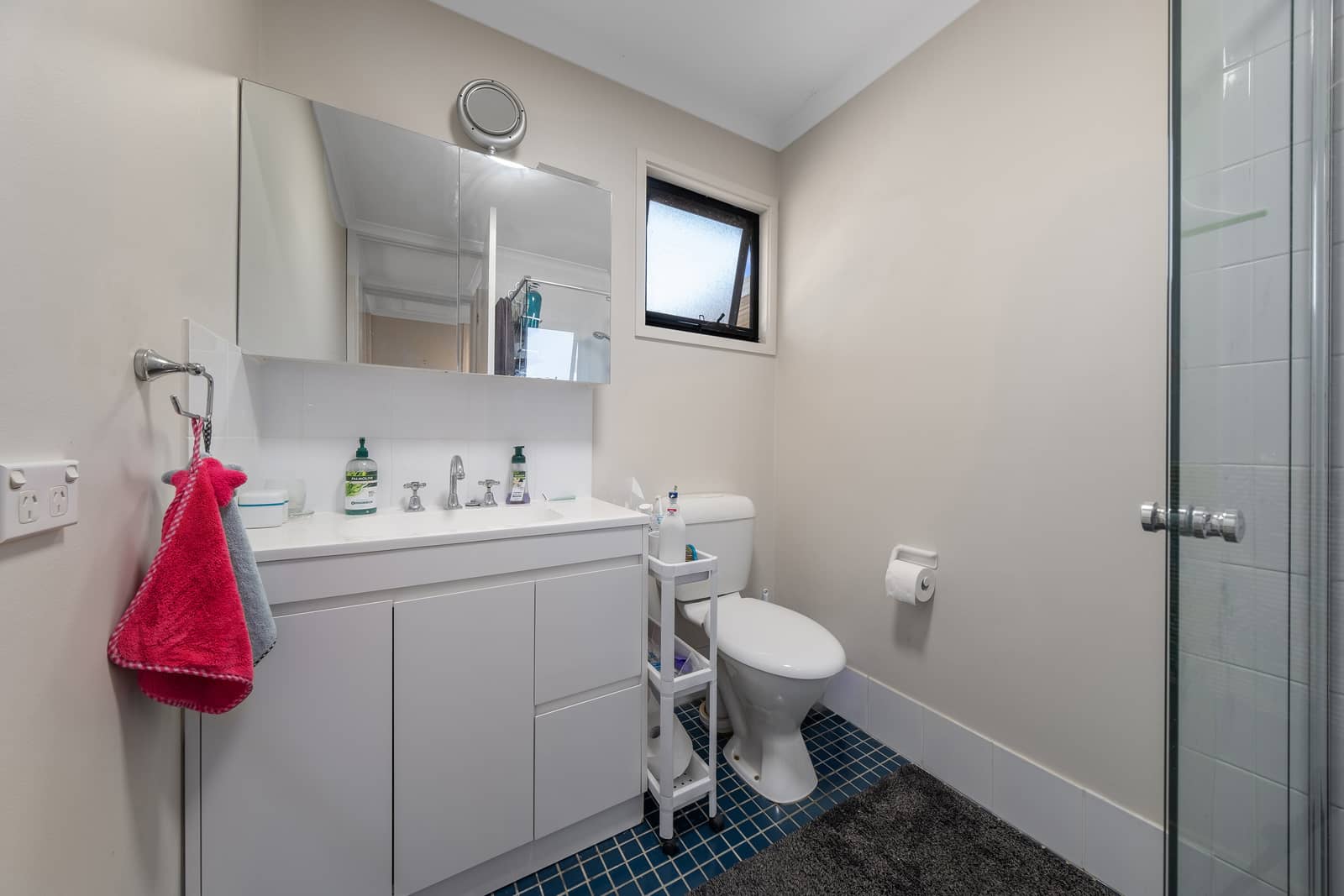 A clean bathroom with a toilet, sink, and shower, featuring blue floor tiles and a large mirrored cabinet.