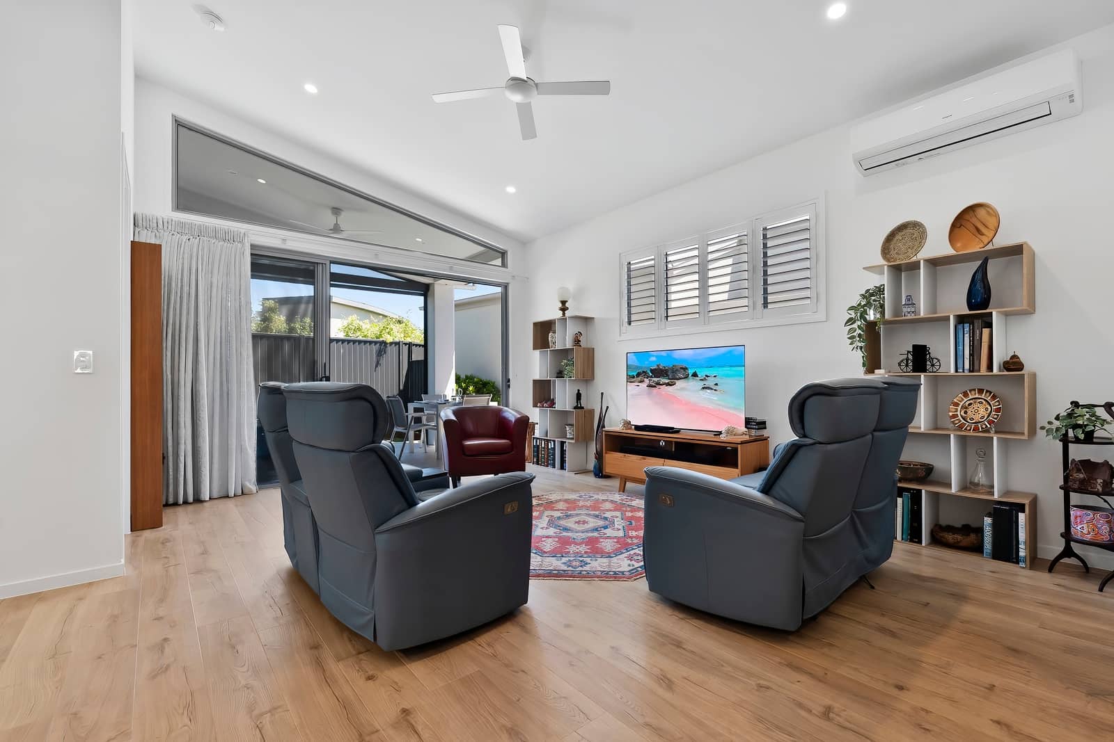 Bright living room of an Ingenia Lifestyle home with wood floors, recliners, TV, and glass doors to an outdoor patio.