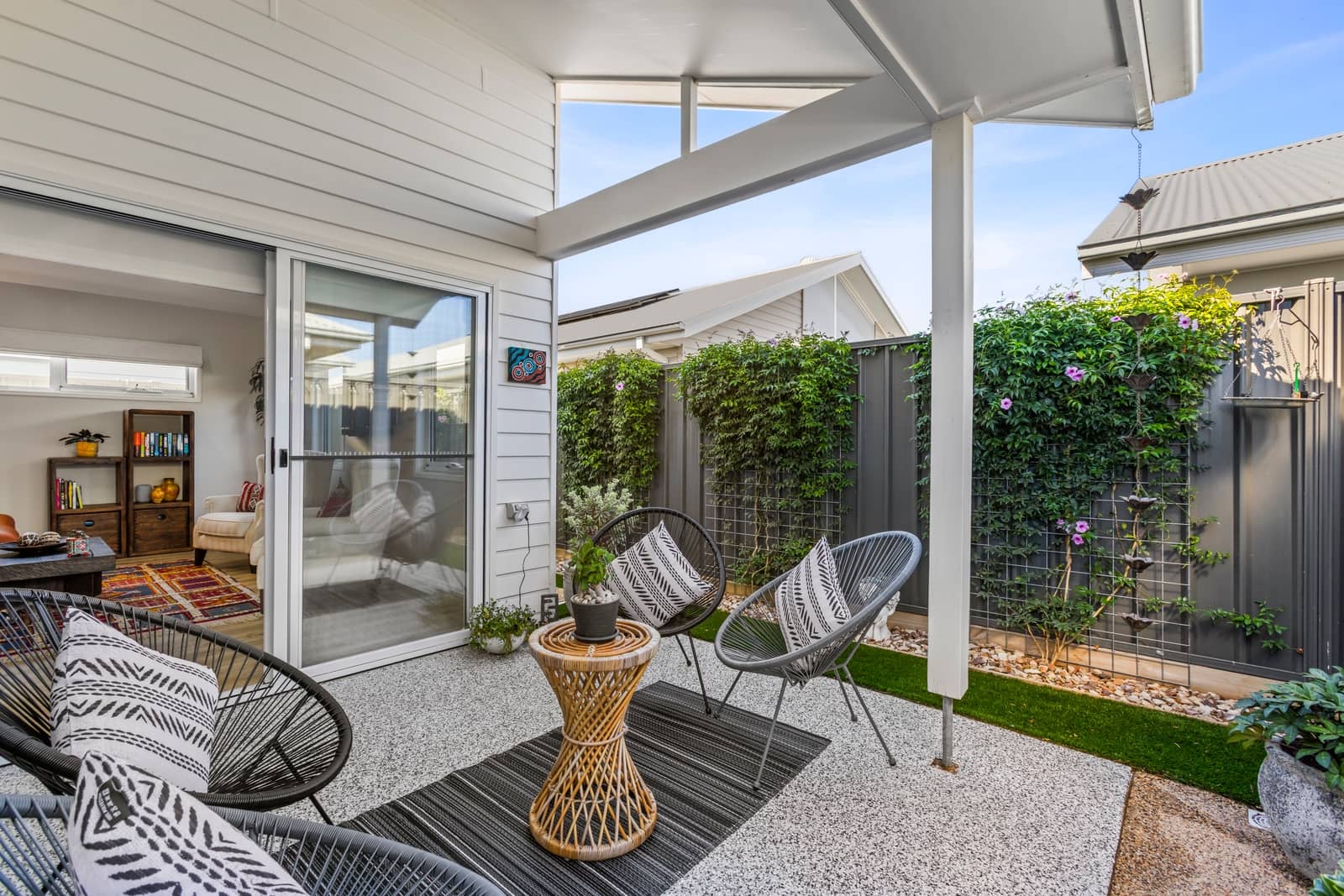 An outdoor patio area with two modern chairs, a small woven table, and a colorful rug.