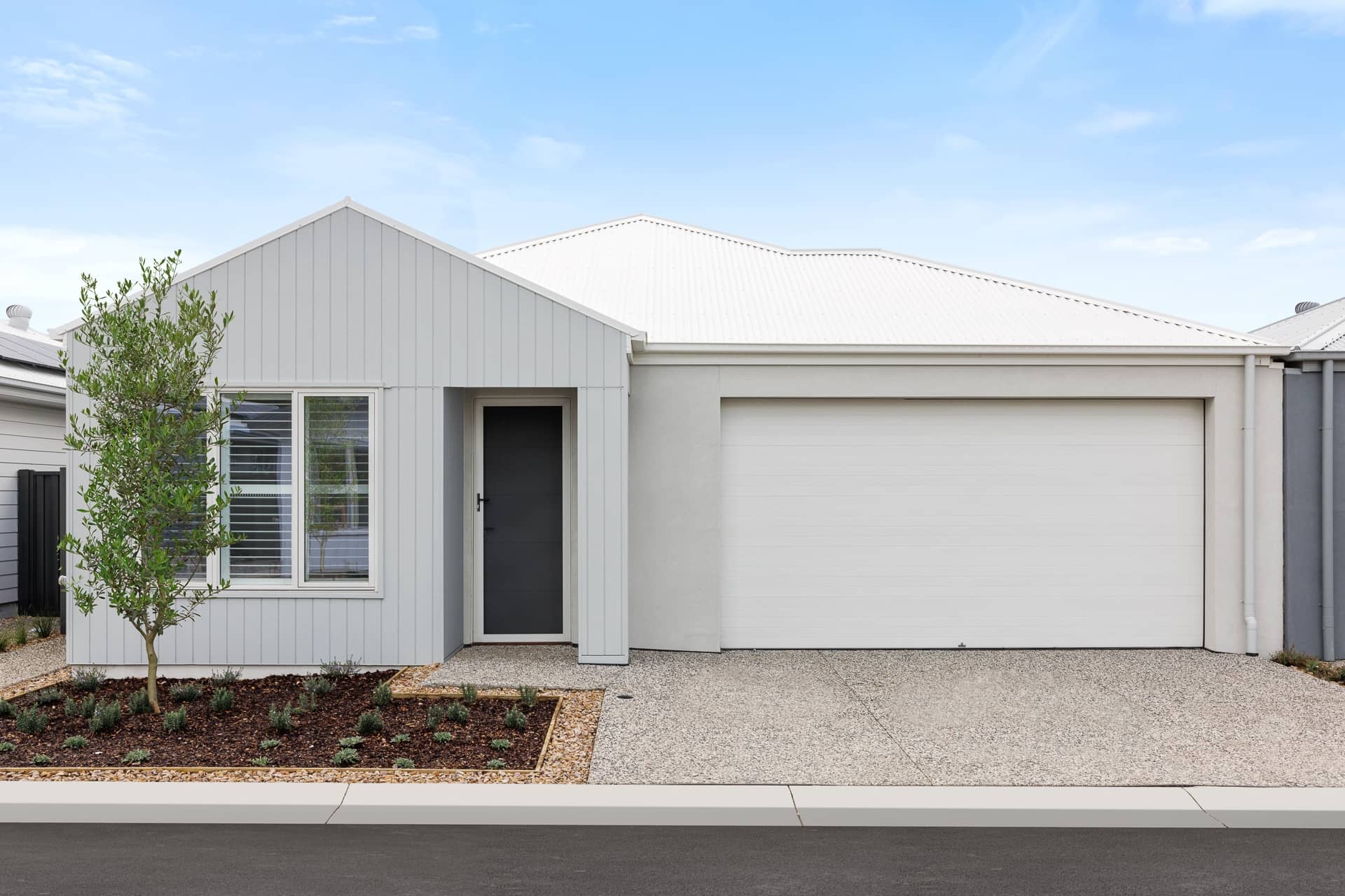 Exterior of a modern, light-grey Ingenia Lifestyle home with a white garage, dark front door, and low-maintenance garden.