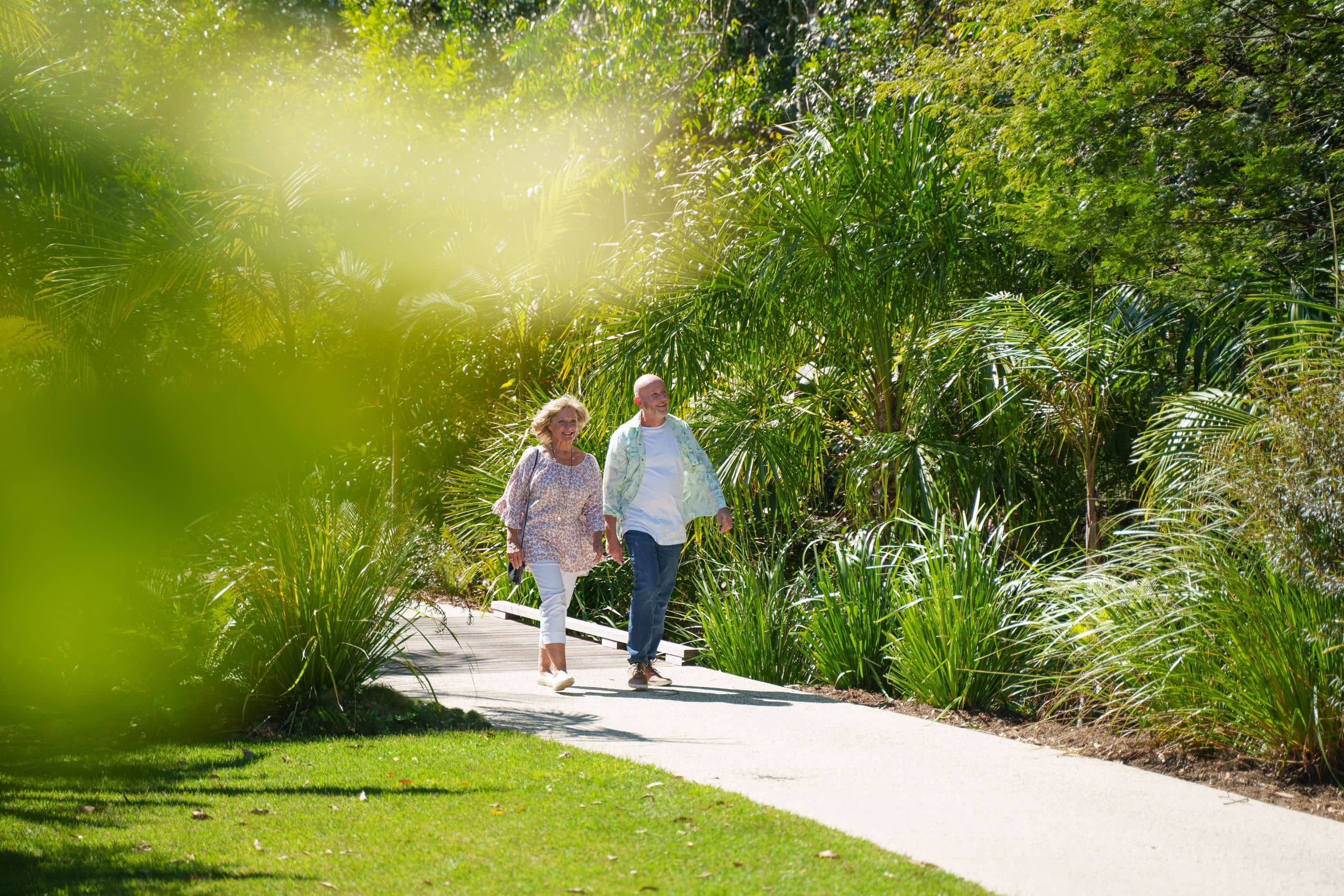 Couple holding hands walking down a green leafy path.