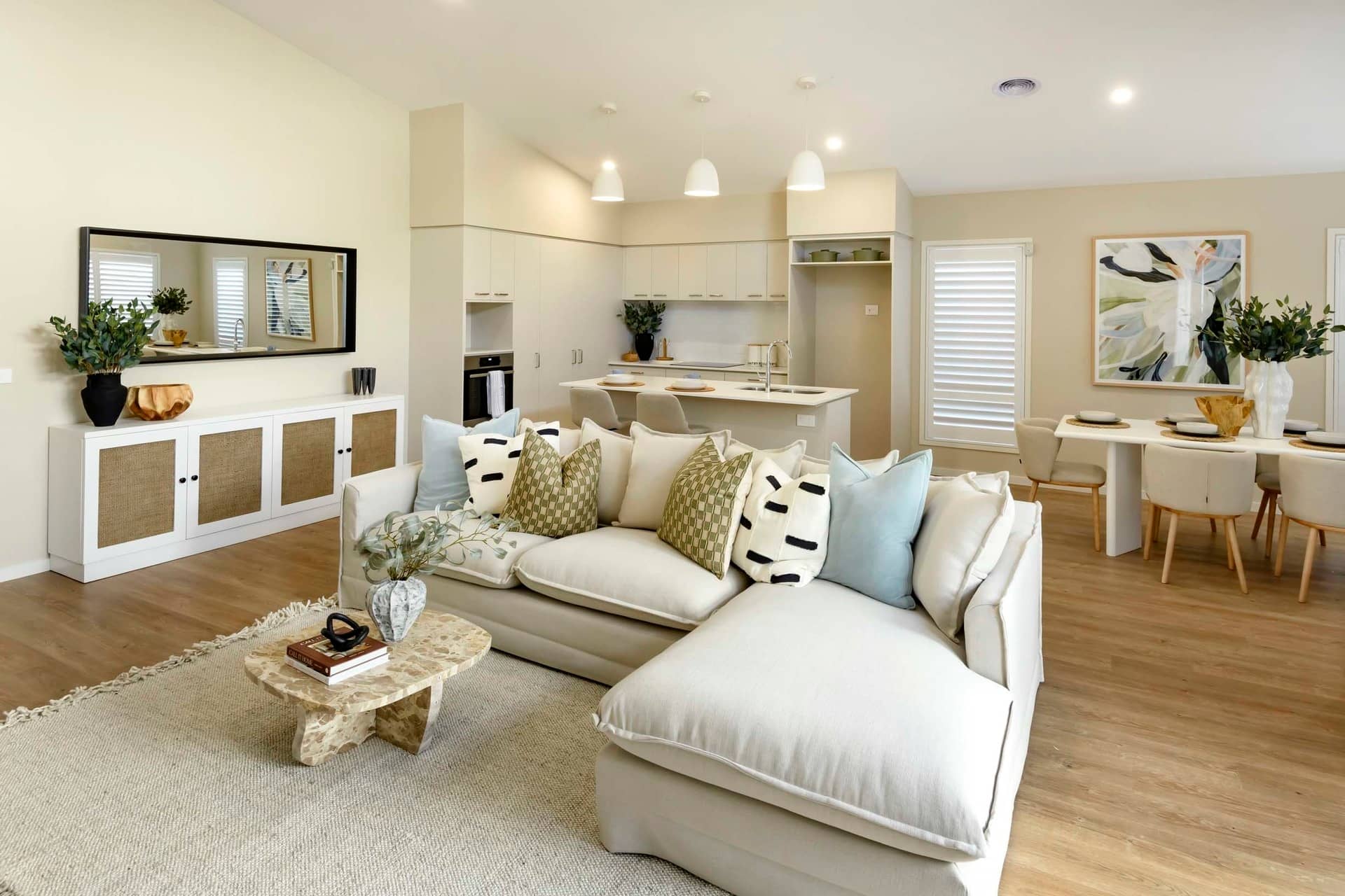 A neutral-toned, open-plan living, dining and kitchen area with a large sectional sofa and a dining table.