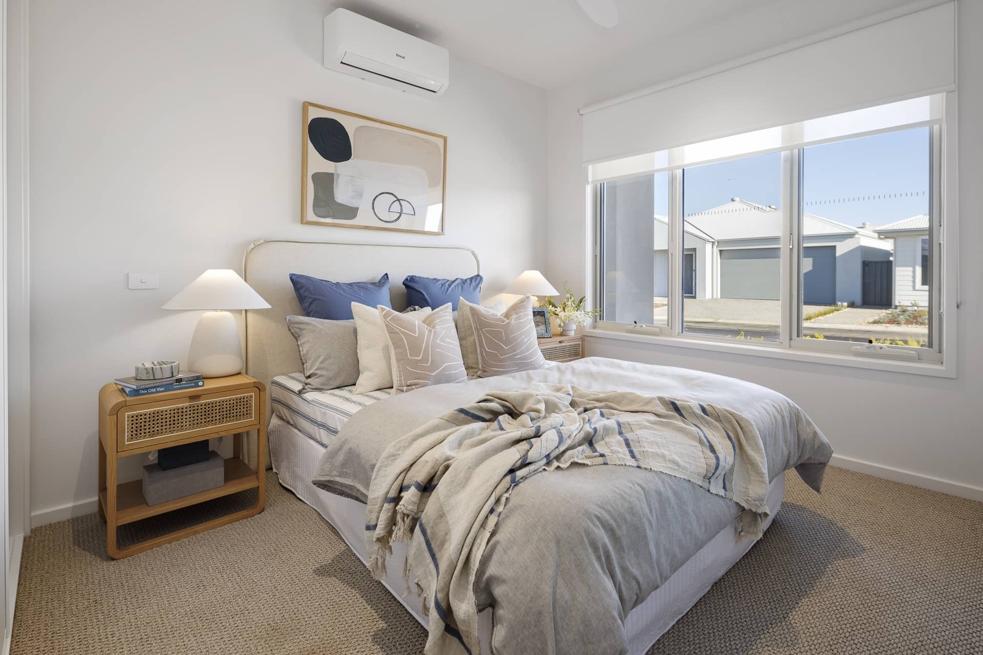 Bright bedroom in an Ingenia Lifestyle home, with a queen bed, bedside tables, wall art, and a window view of other community homes.