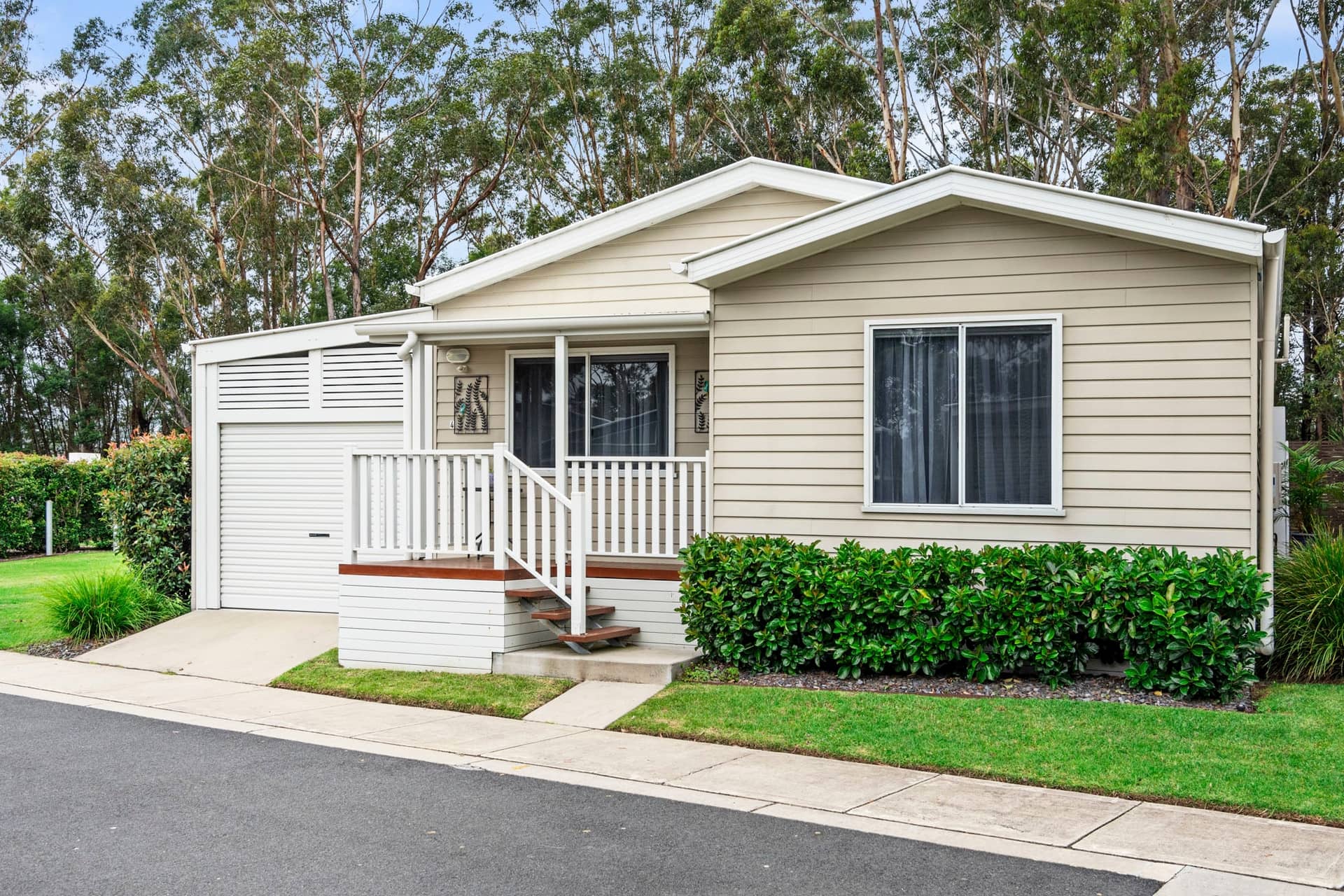 A beige Ingenia Lifestyle land lease home with a front porch, attached garage, and landscaped yard.