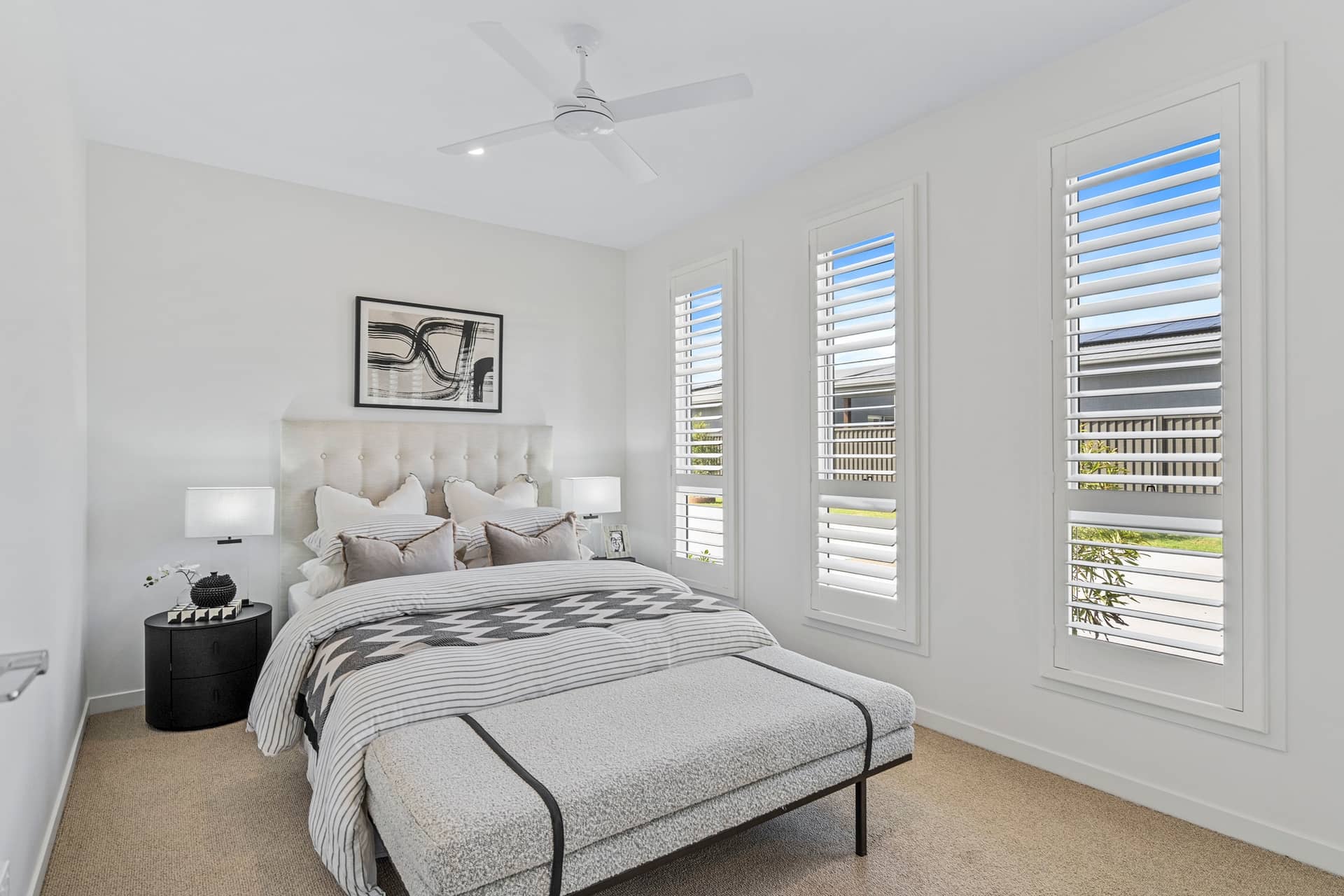 A bright bedroom with a bed, bedside table, and ceiling fan.