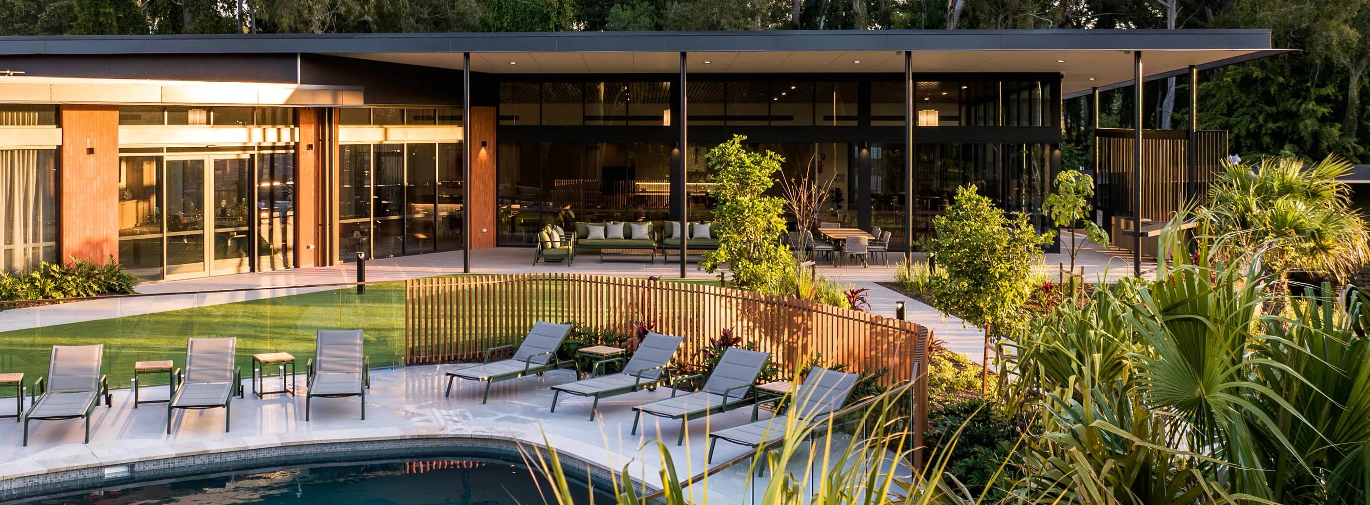 Modern community building with glass facade, outdoor pool, sun loungers, and landscaped gardens.