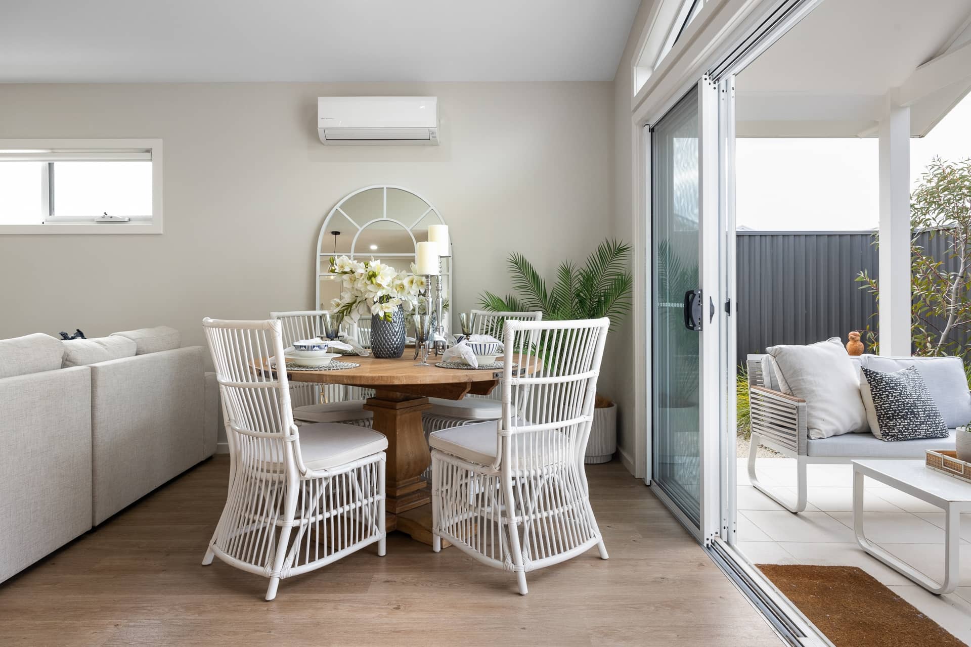 Dining area with white rattan chairs and a wooden table, opening to an outdoor patio.