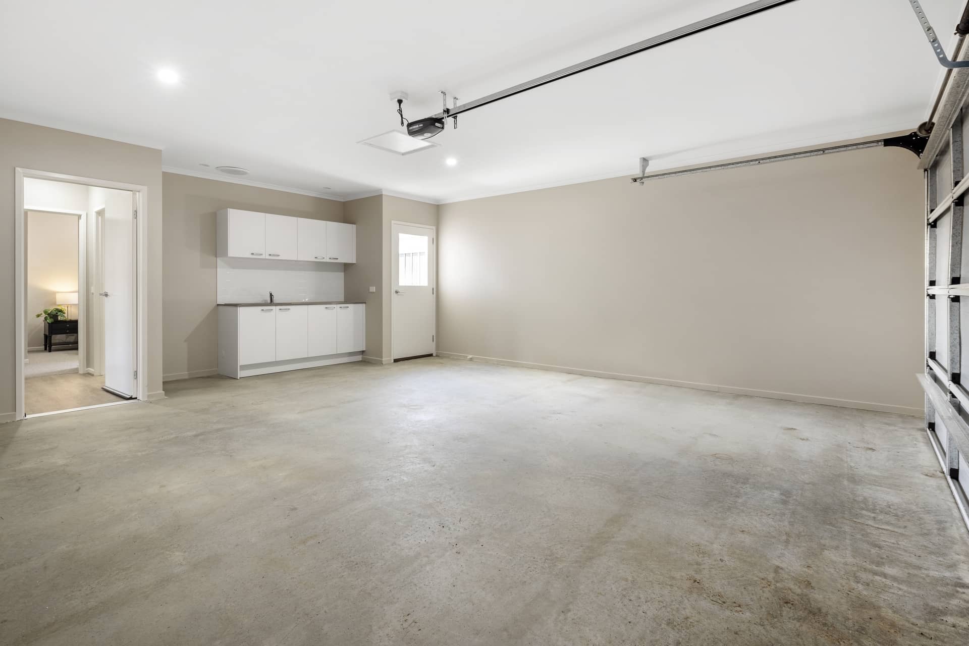 Empty garage with concrete floor, beige walls, white cabinetry, and a garage door track.
