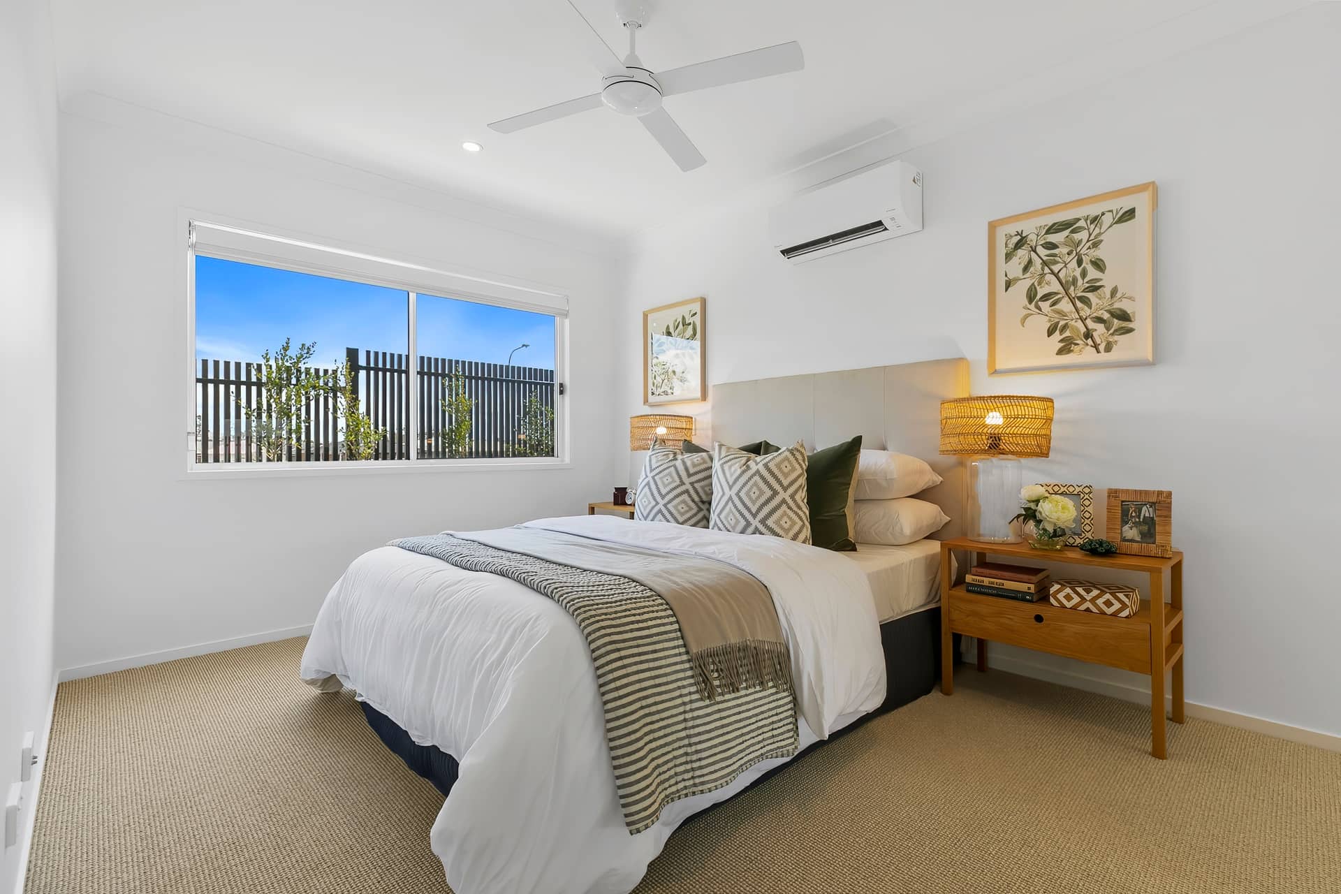 Modern bedroom in an Ingenia Lifestyle home with a bed, wooden bedside table, large window, ceiling fan, and air conditioning unit.