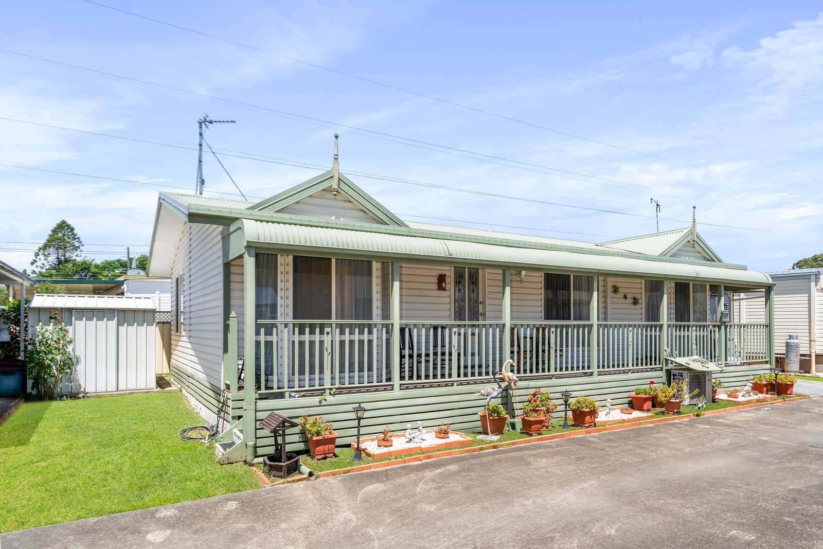 An Ingenia Lifestyle land lease home with a wide porch, white siding, and green trim. Potted plants line the front yard.