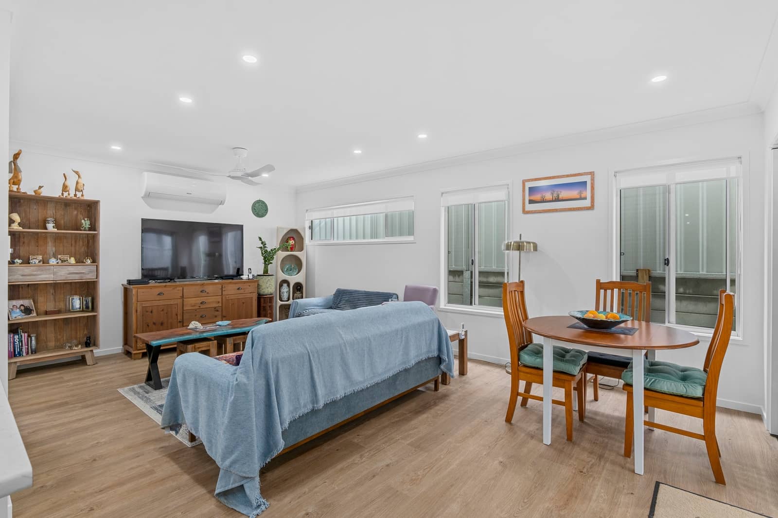 An open-plan living and dining area in an Ingenia Lifestyle home, featuring a sofa, TV, wooden dining table, and wood-look flooring.