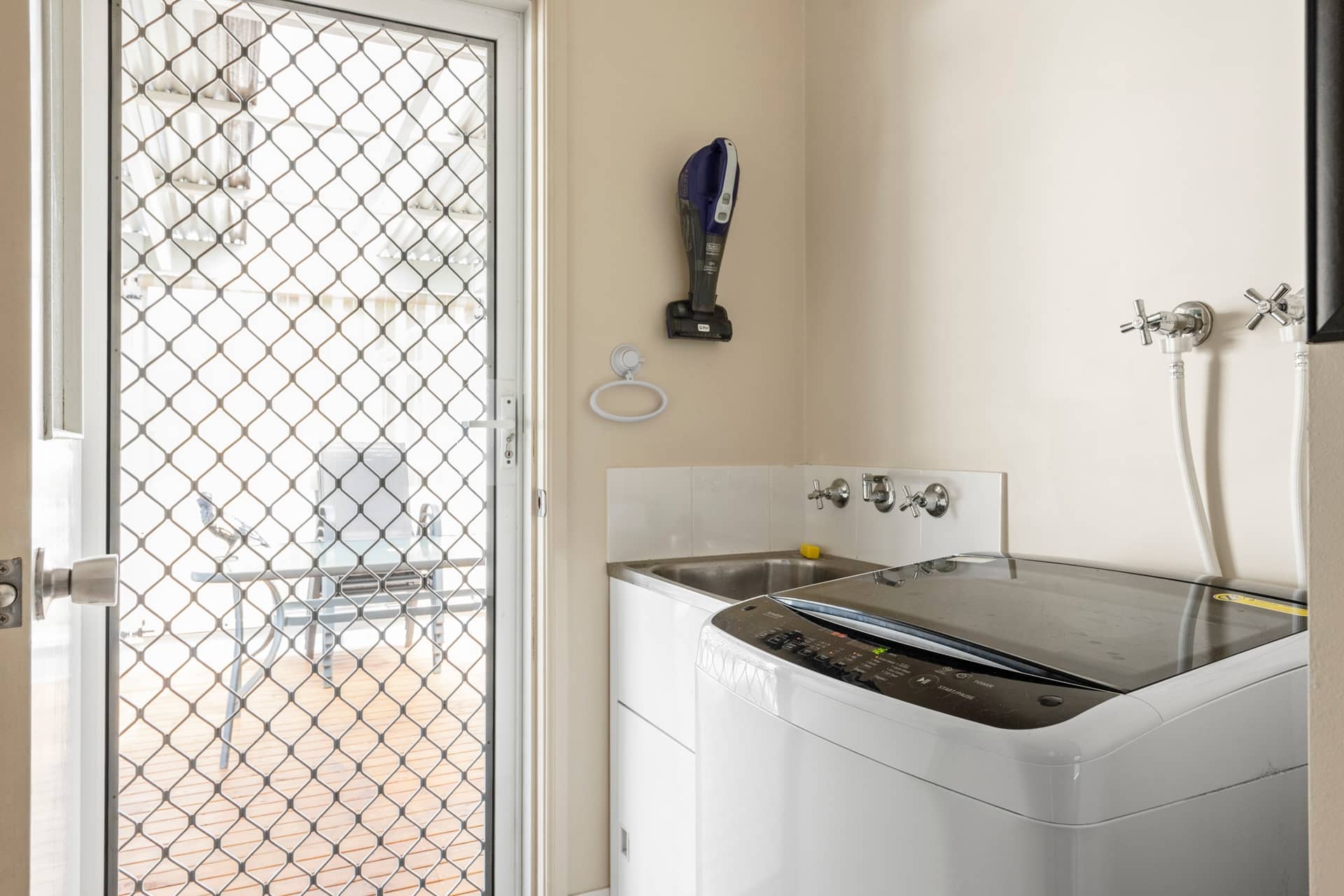 Laundry room in an Ingenia Lifestyle home with a washing machine, utility sink, and a security screen door to a deck.