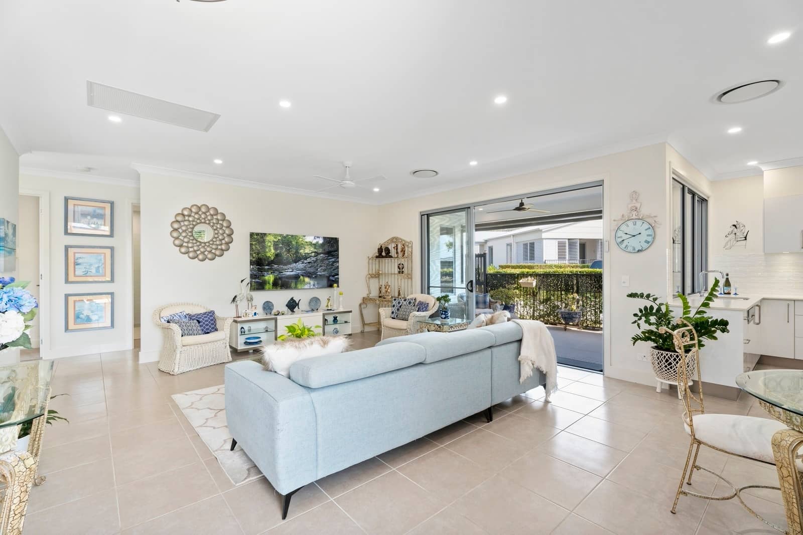 Bright, open-plan living room with tiled floors, a blue sofa, and sliding doors to a patio overlooking an Ingenia Lifestyle community.