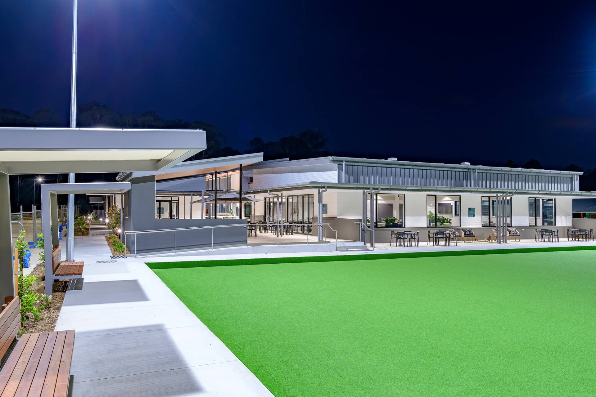 Modern Ingenia Lifestyle shared amenities building with illuminated outdoor seating, overlooking a green lawn at night.