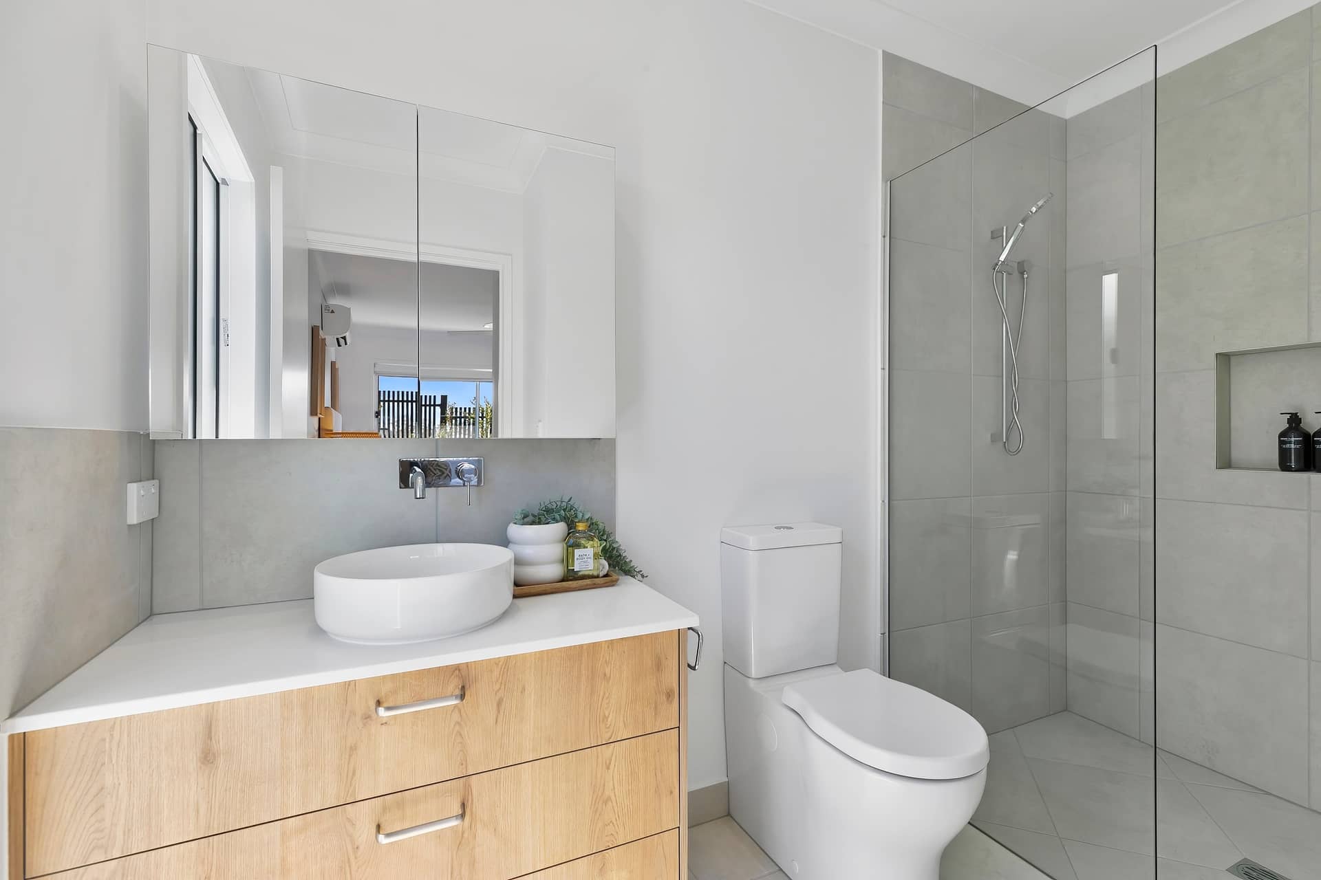 Modern bathroom in an Ingenia Lifestyle home, featuring a wood vanity, white basin, toilet, and walk-in shower.