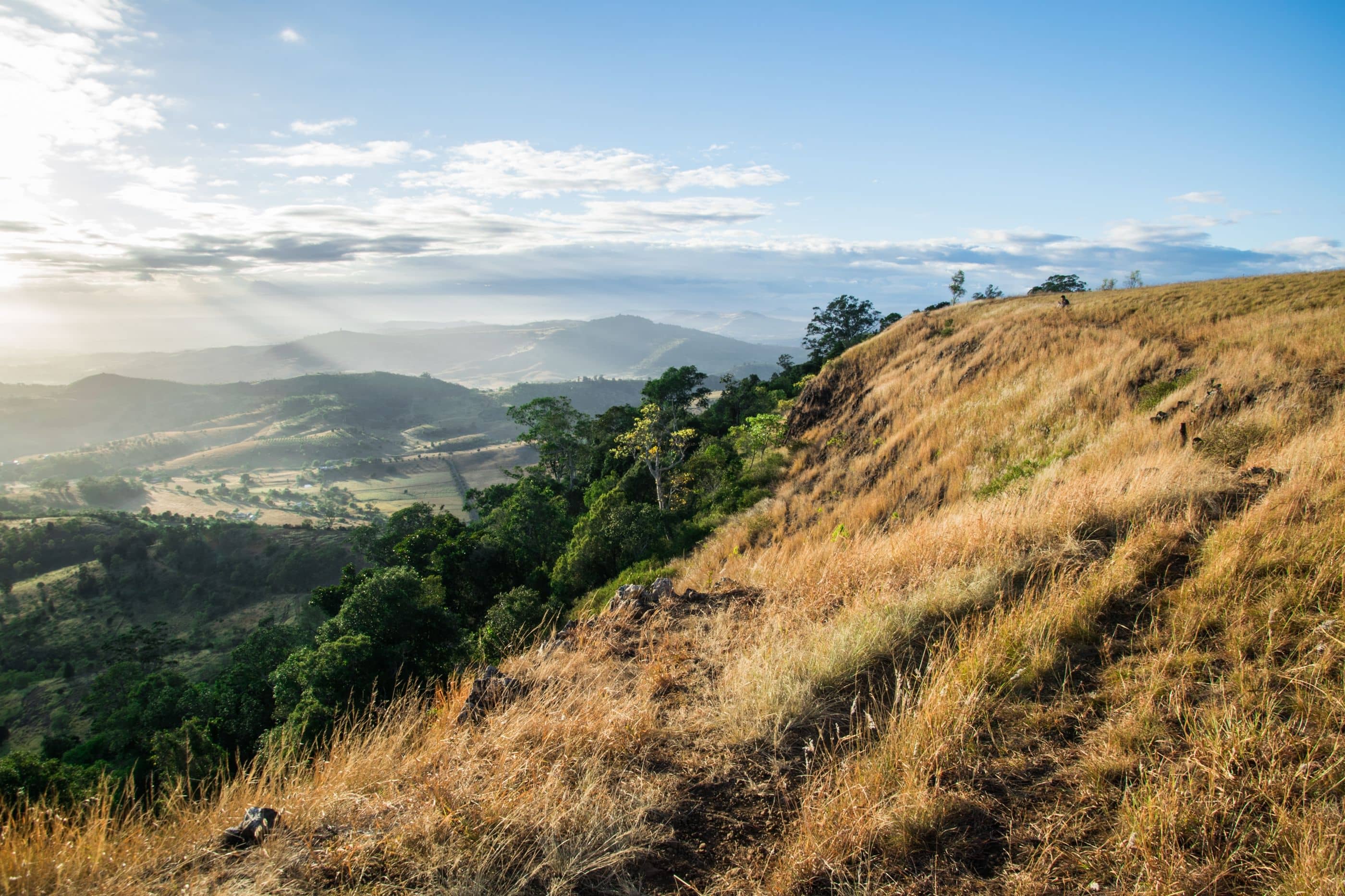 Sunlight streams through clouds over rolling hills and a grassy slope.