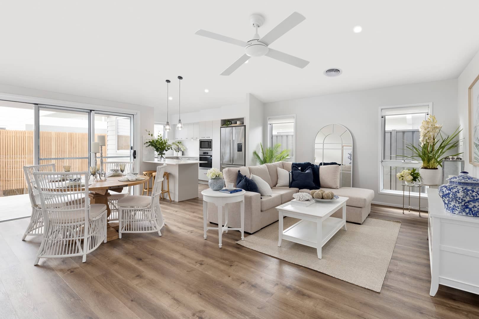 Open plan living and dining area with white wicker chairs, modern kitchen, and beige sectional sofa.