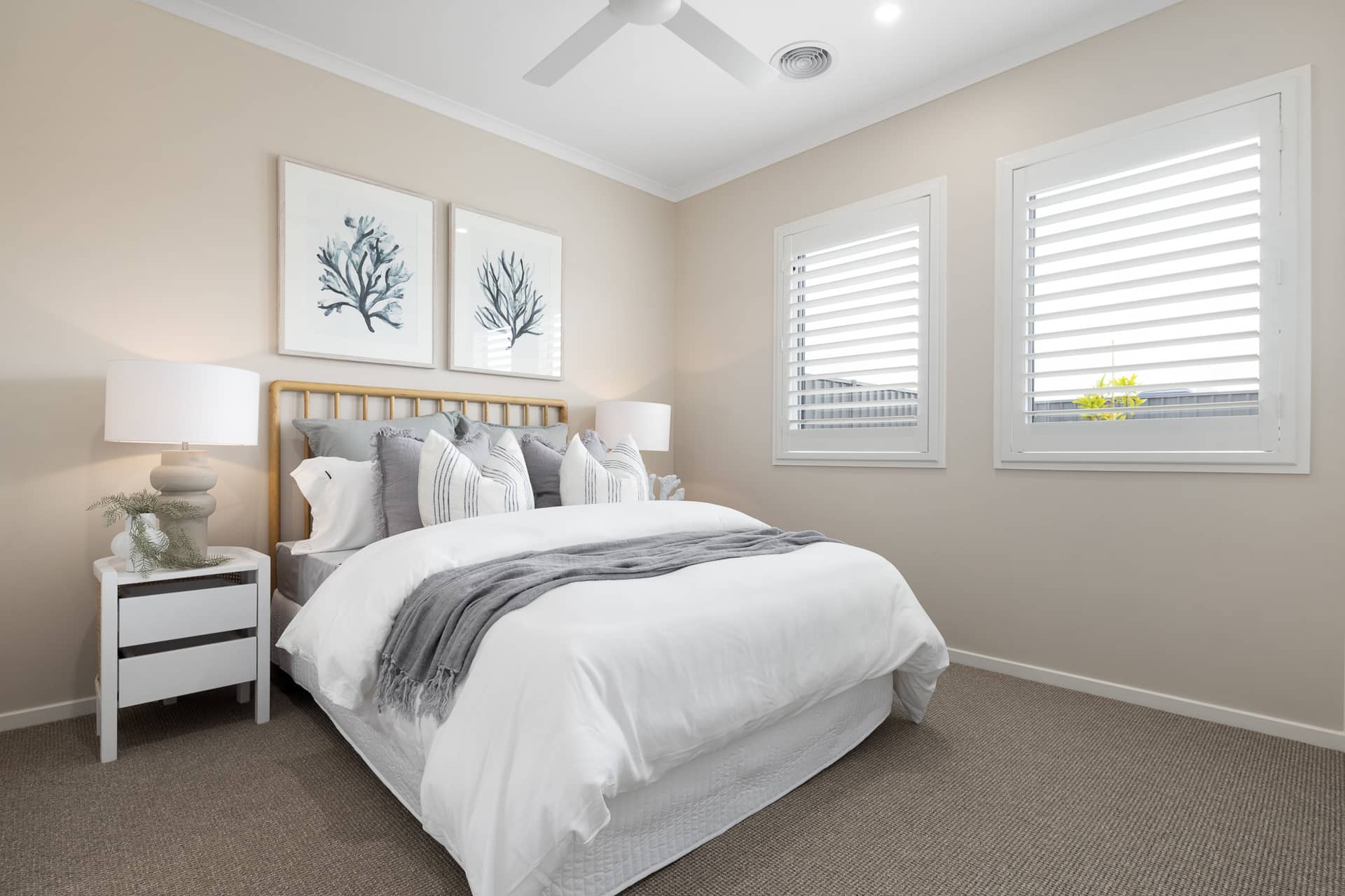 A neatly made bed with white linen and grey throws in a neutral bedroom with two framed coral prints.