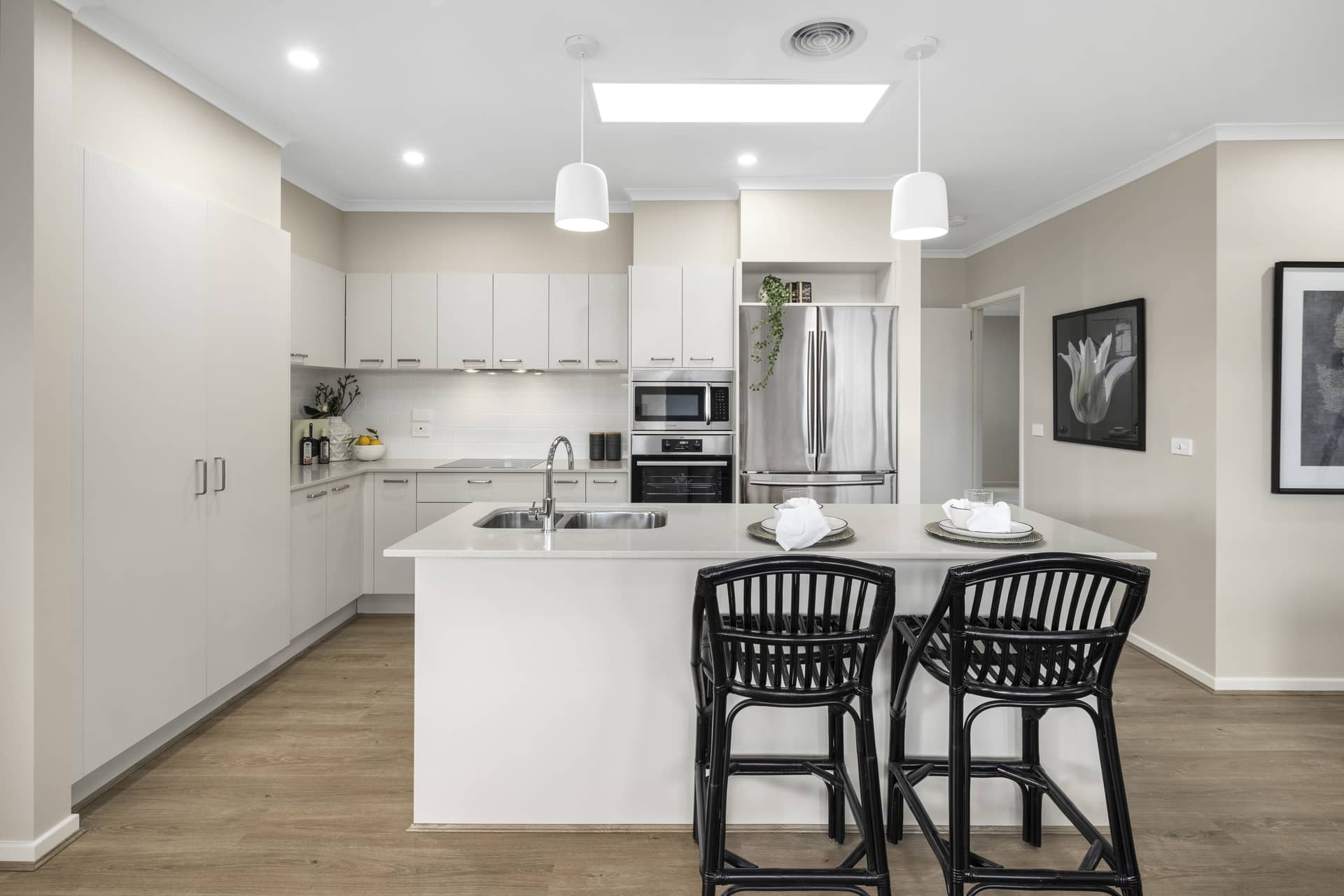 Modern kitchen with white cabinetry, a central island with bar stools, and stainless steel appliances in an Ingenia Lifestyle community.