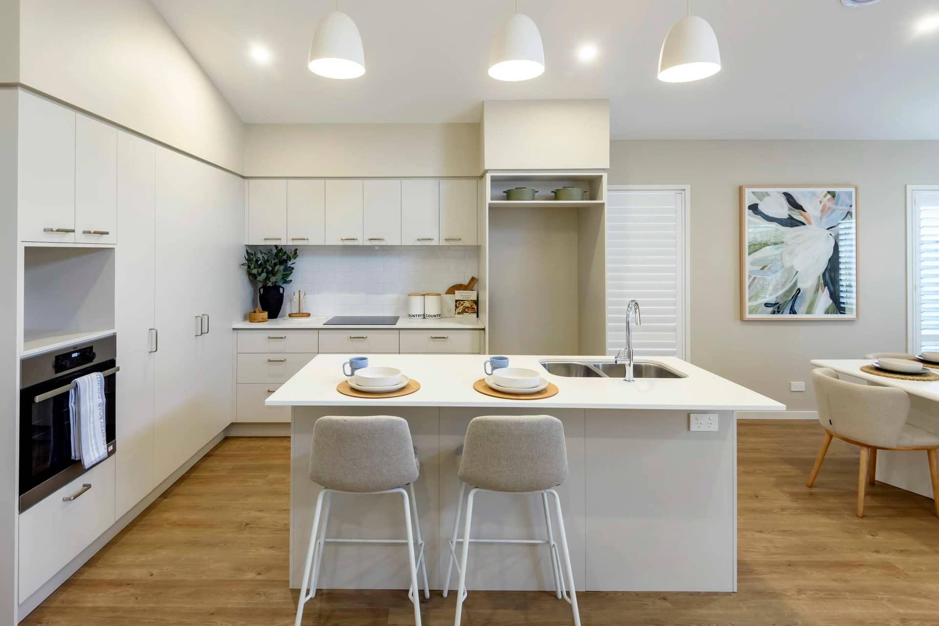 Modern kitchen island with bar stools, white cabinetry, and artwork in an Ingenia Lifestyle community.