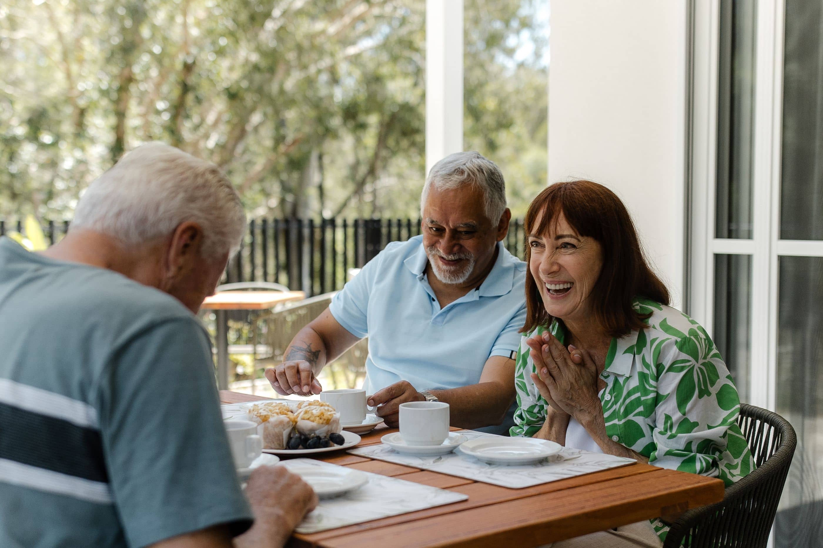 Smiling residents enjoy coffee and muffins together on an Ingenia Lifestyle community patio.