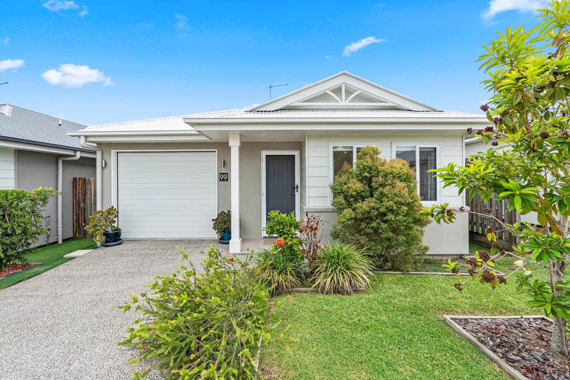 A grey land lease home with a white garage door and white trim, under a blue sky with white clouds.