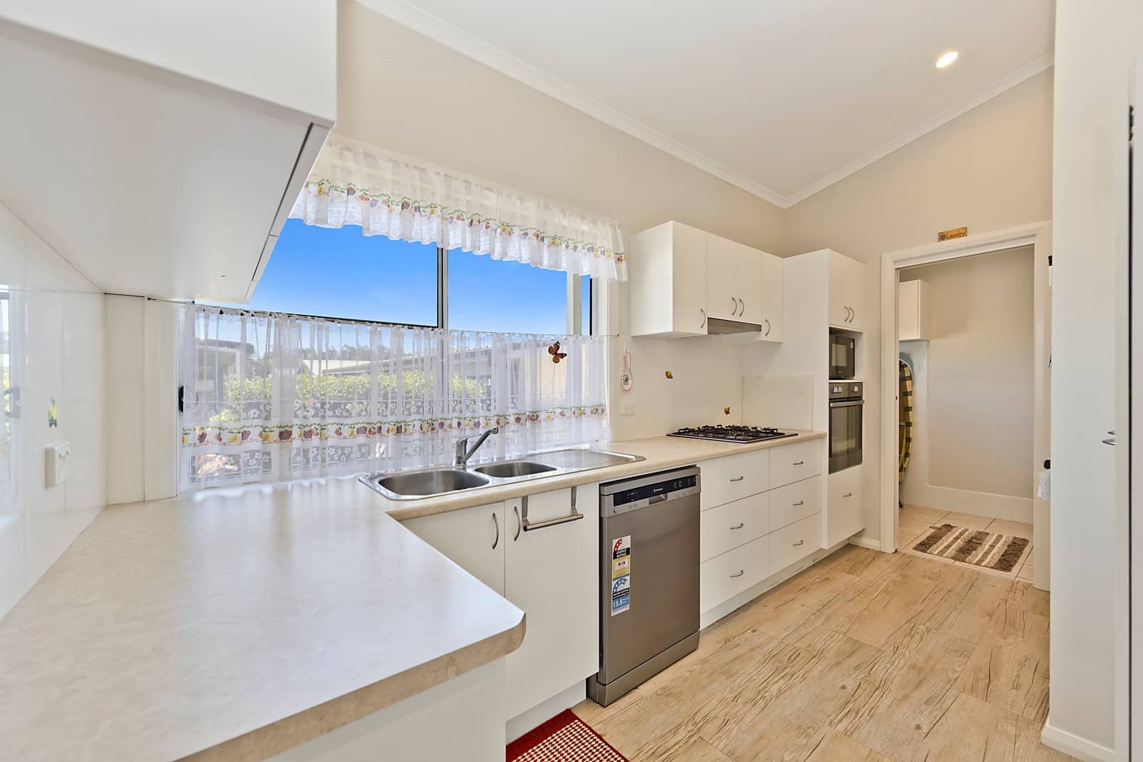 Bright kitchen in an Ingenia Lifestyle home with white cabinetry, light countertops, double sink, gas cooktop, oven, and dishwasher.