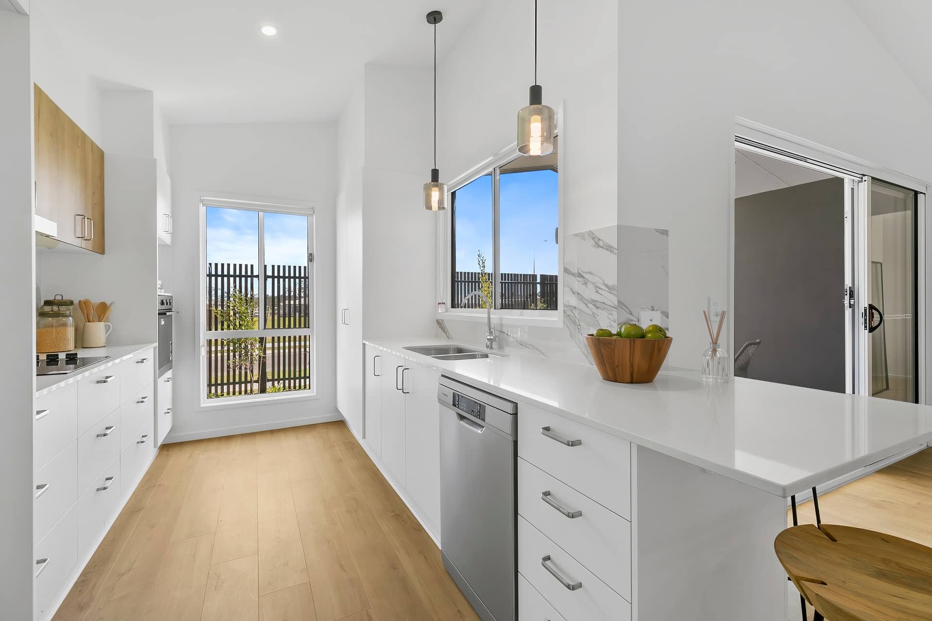 A bright, modern kitchen in an Ingenia Lifestyle home with white cabinetry, light timber flooring, stainless steel appliances, and a window.