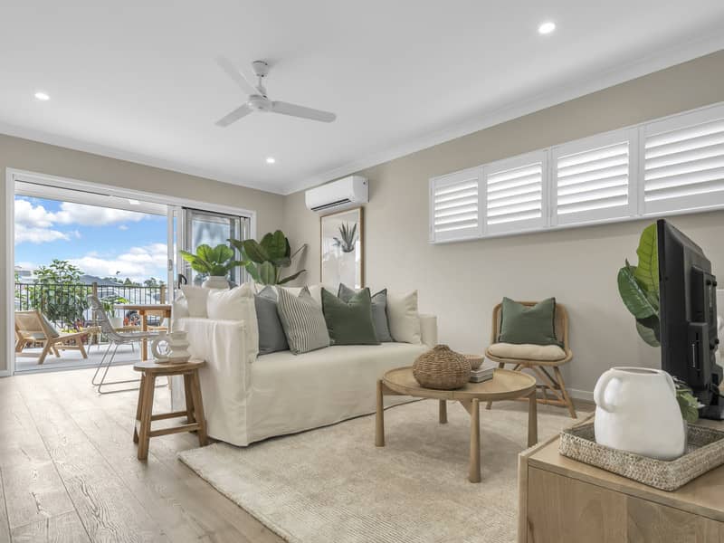 A light and airy living room with a white sofa, rattan chairs, and a coffee table, opening onto a balcony with outdoor seating.