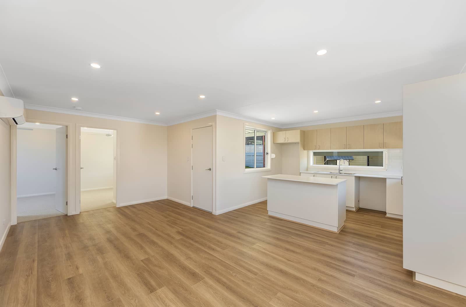 Open-plan kitchen and living area with wood-look flooring, white walls, light cabinetry, and an island bench in an Ingenia Lifestyle home.