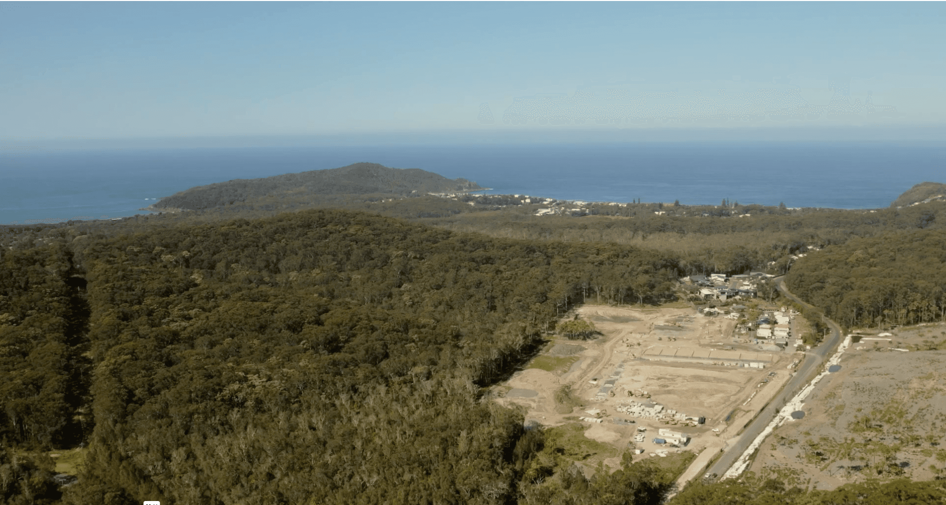 Aerial view of an Ingenia Lifestyle development site, with cleared land, forest, a coastal town, and the ocean.