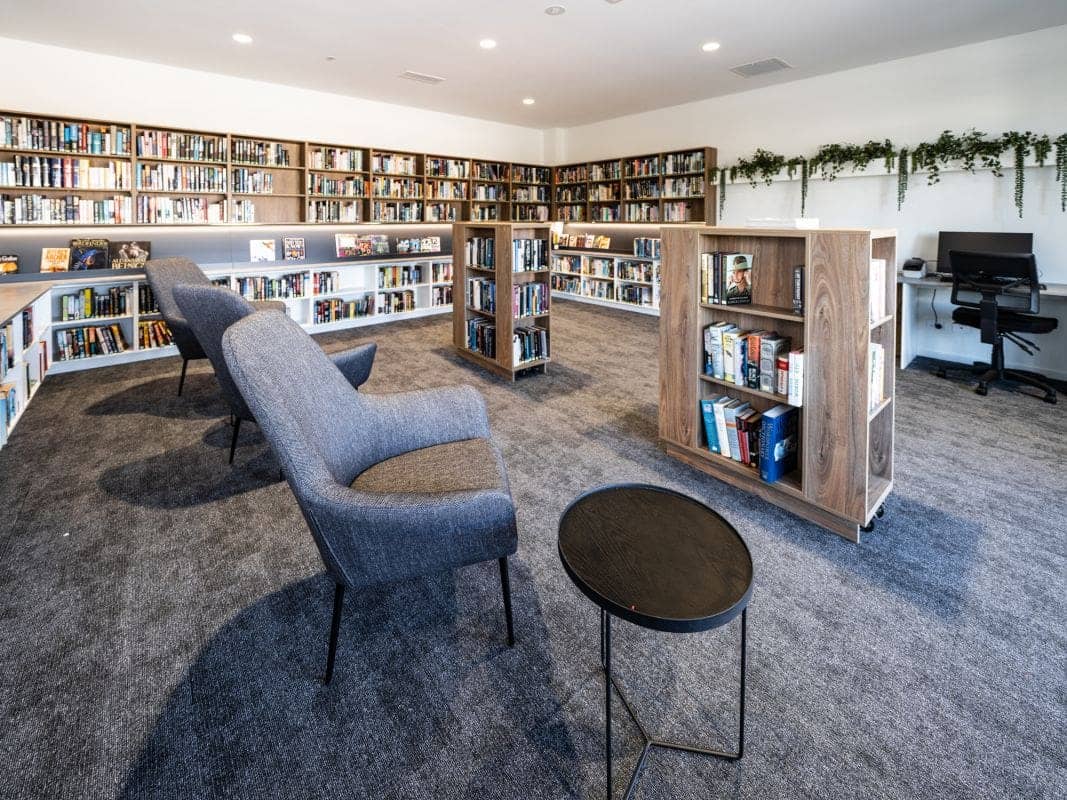 Comfortable seating area with bookshelves and a computer in an Ingenia Lifestyle community library.