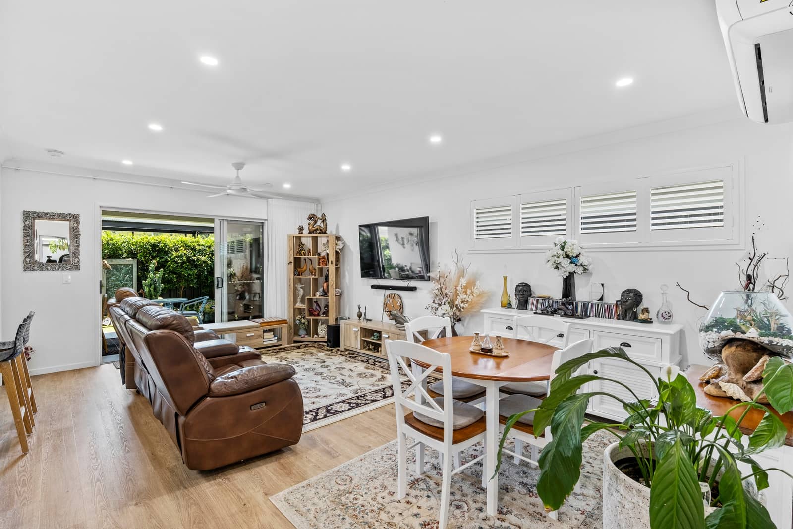 Open-plan living and dining area in an Ingenia Lifestyle home with light wood floors, a brown sofa, and patio access.