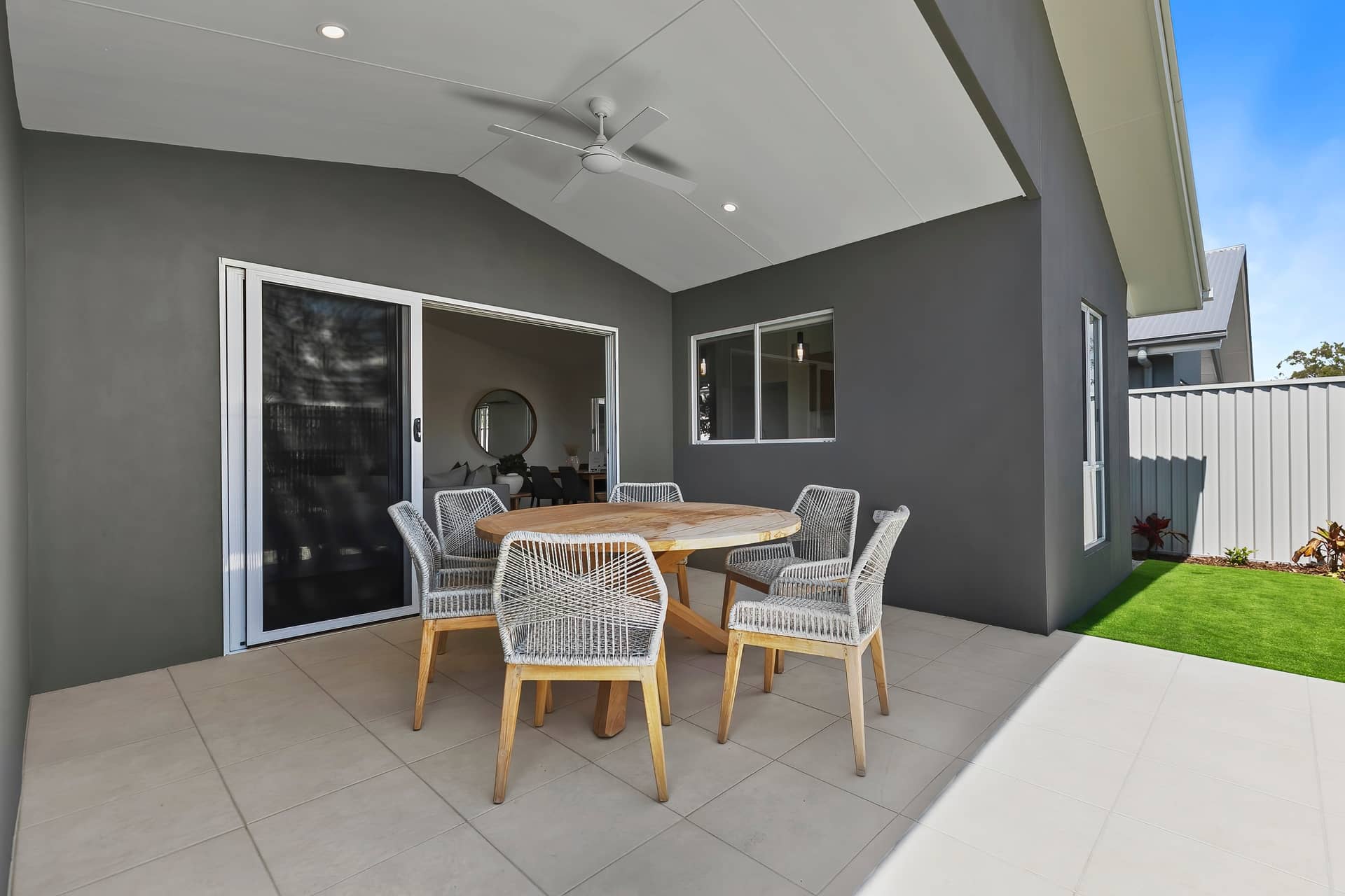 Covered patio of an Ingenia Lifestyle home with a round wooden table, six woven chairs, tiled floor, and a small lawn.
