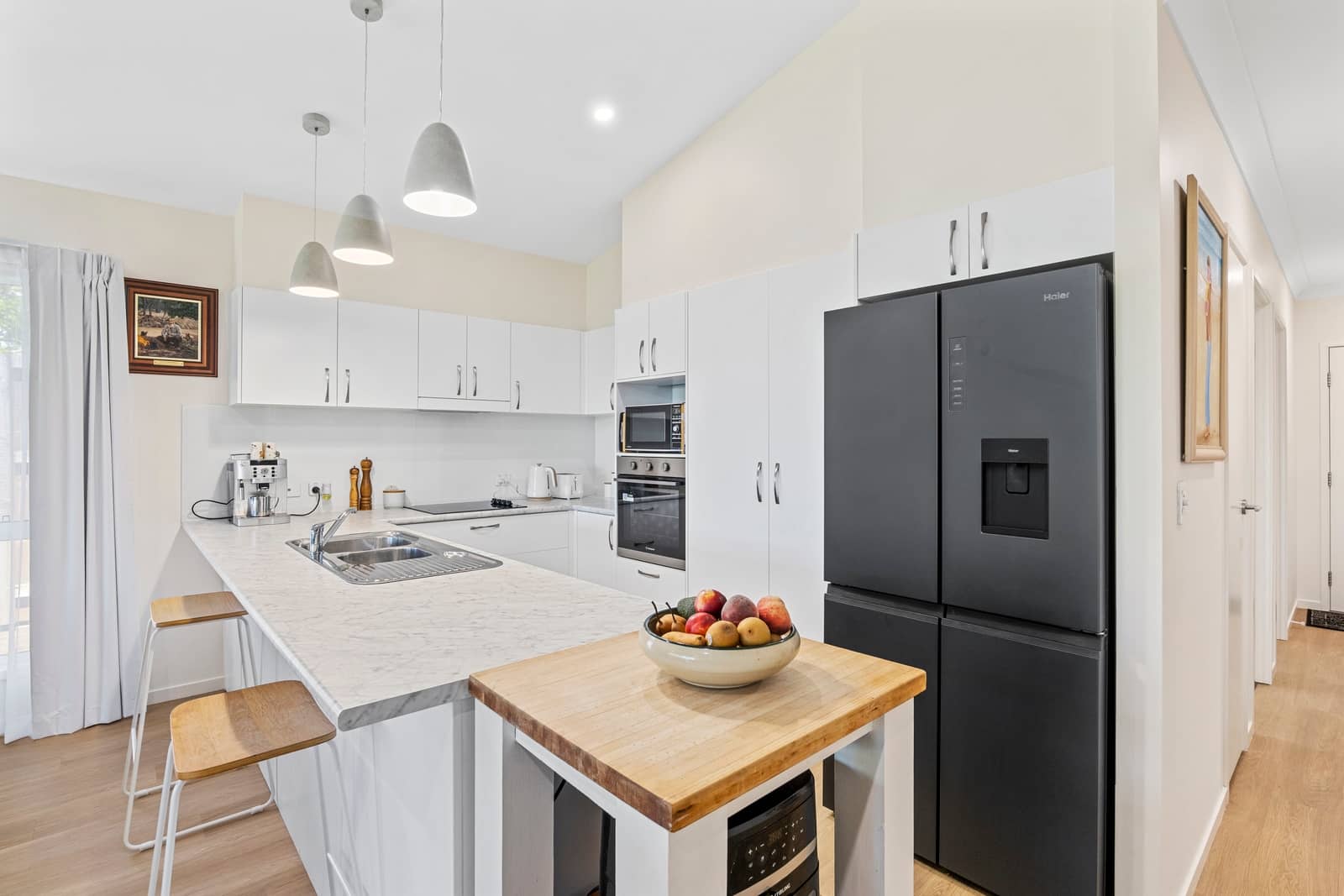 Modern kitchen with white cabinetry, marble-look benchtops, and a black Haier refrigerator in an Ingenia Lifestyle community.