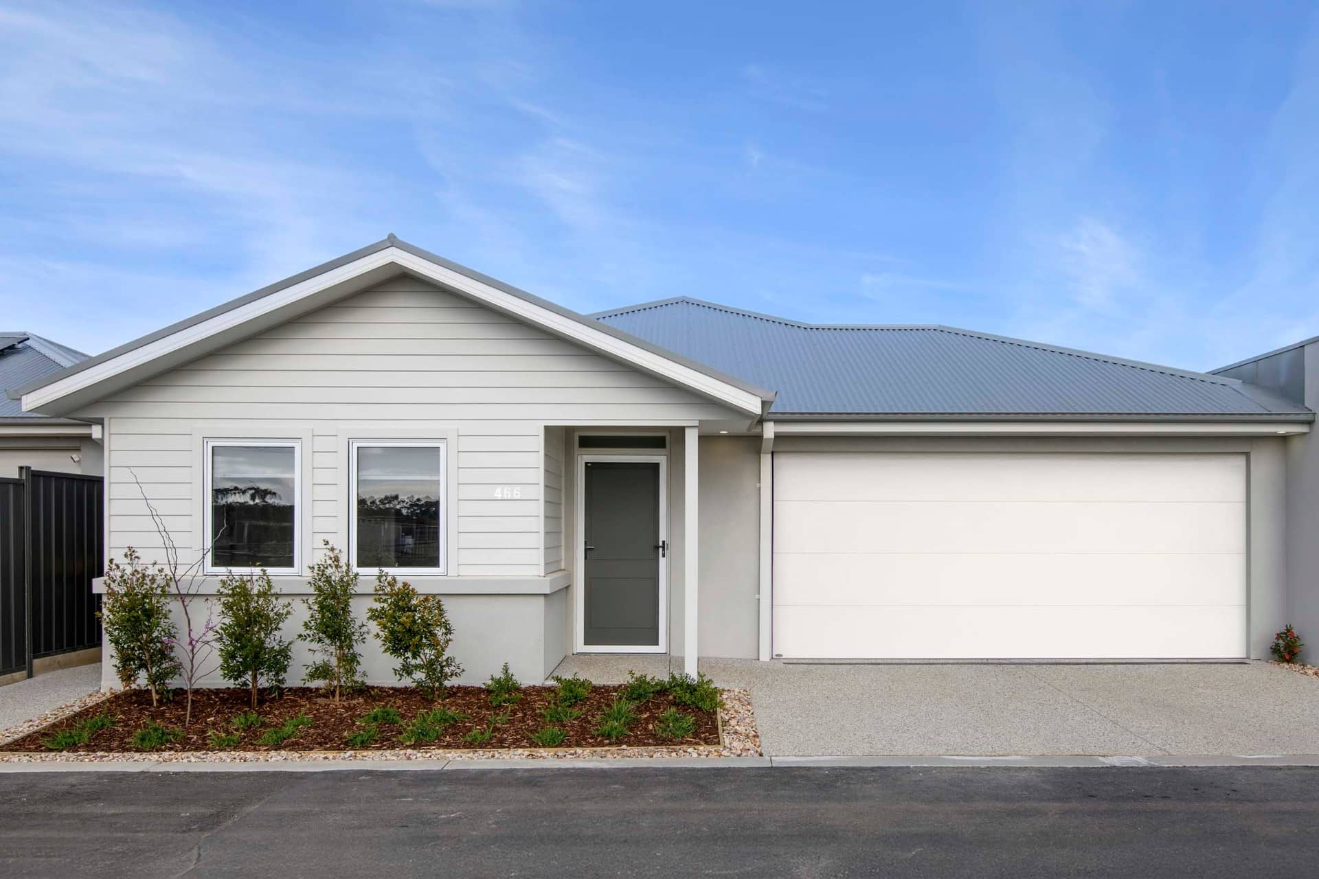 Exterior of a light grey land lease home with a white garage door and a grey pitched roof.