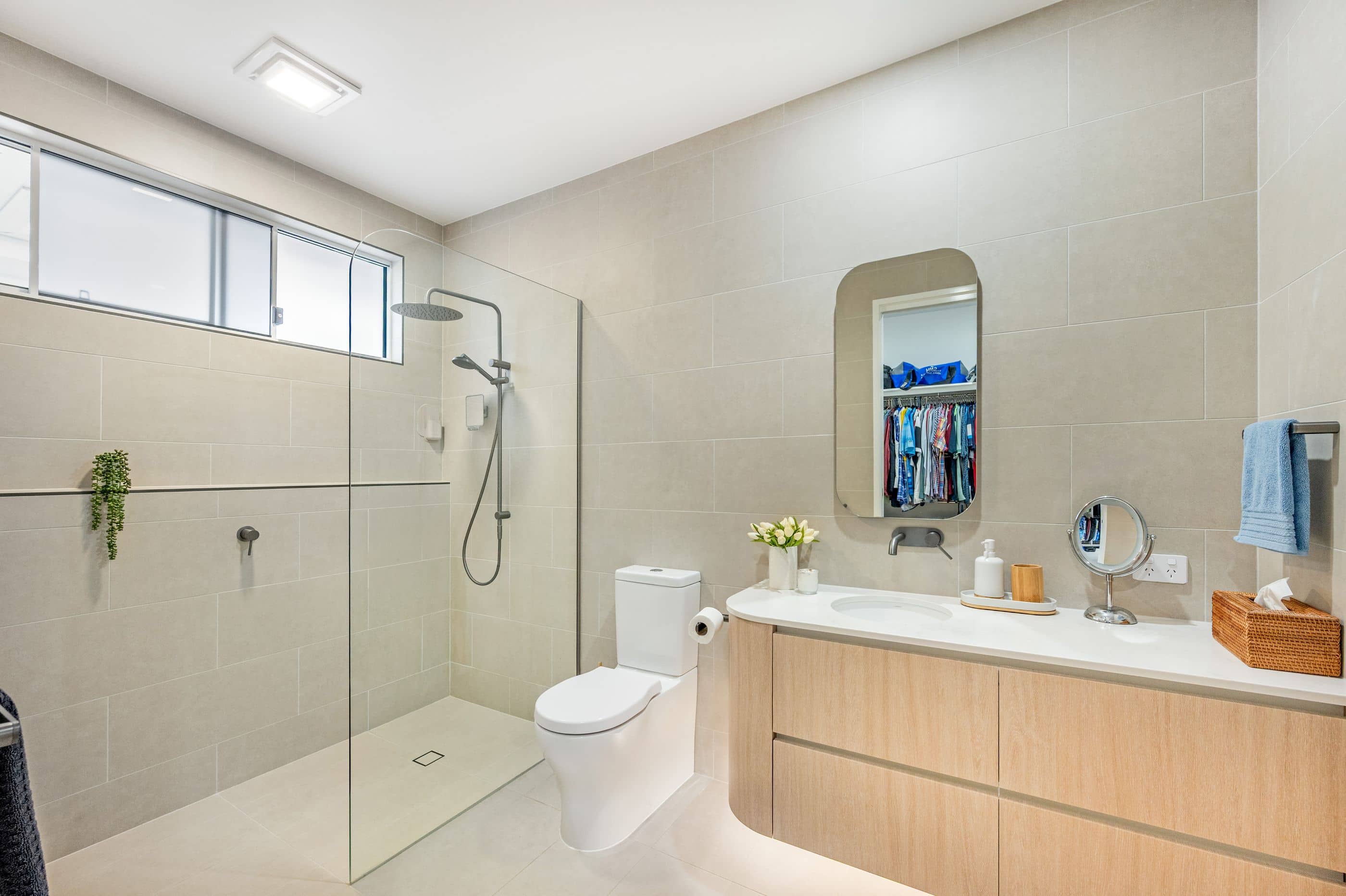 A modern Ingenia Lifestyle bathroom featuring a walk-in shower, toilet, timber vanity, and neutral tiles.