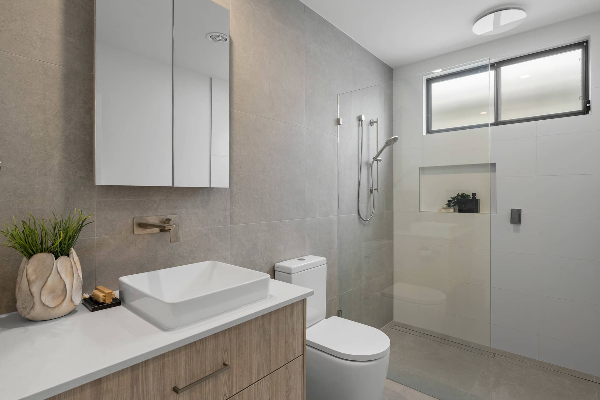 Modern bathroom with wood-look vanity, basin, toilet, and walk-in shower with glass screen, in an Ingenia Lifestyle home.