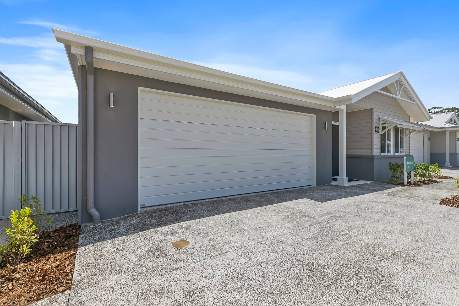 Modern Ingenia Lifestyle home with a white garage door, grey exterior, and aggregate concrete driveway. Low-maintenance living.