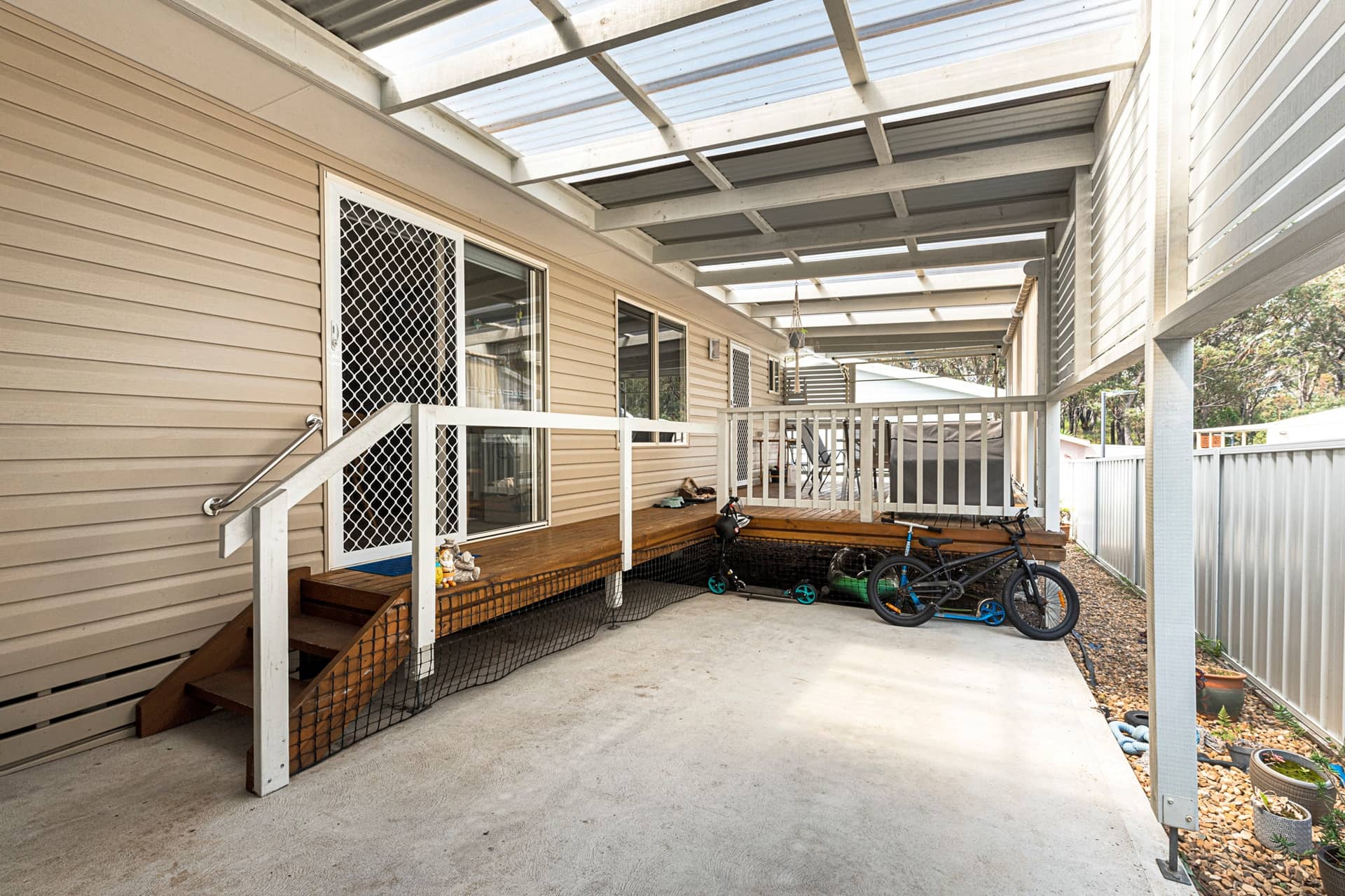 Covered outdoor entertaining area of an Ingenia Lifestyle home, featuring a timber deck, concrete patio, and stairs with a handrail.