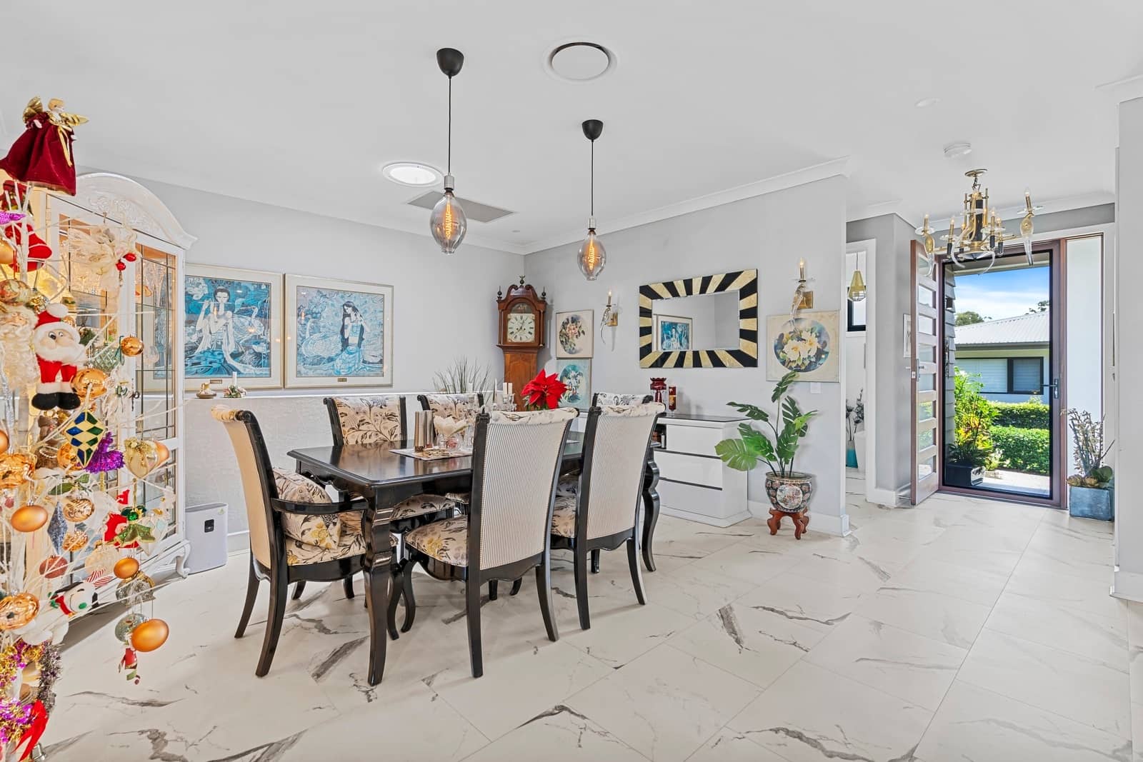 Dining room with a dark wood table and chairs, ornate cabinet, and view to an entryway and garden.