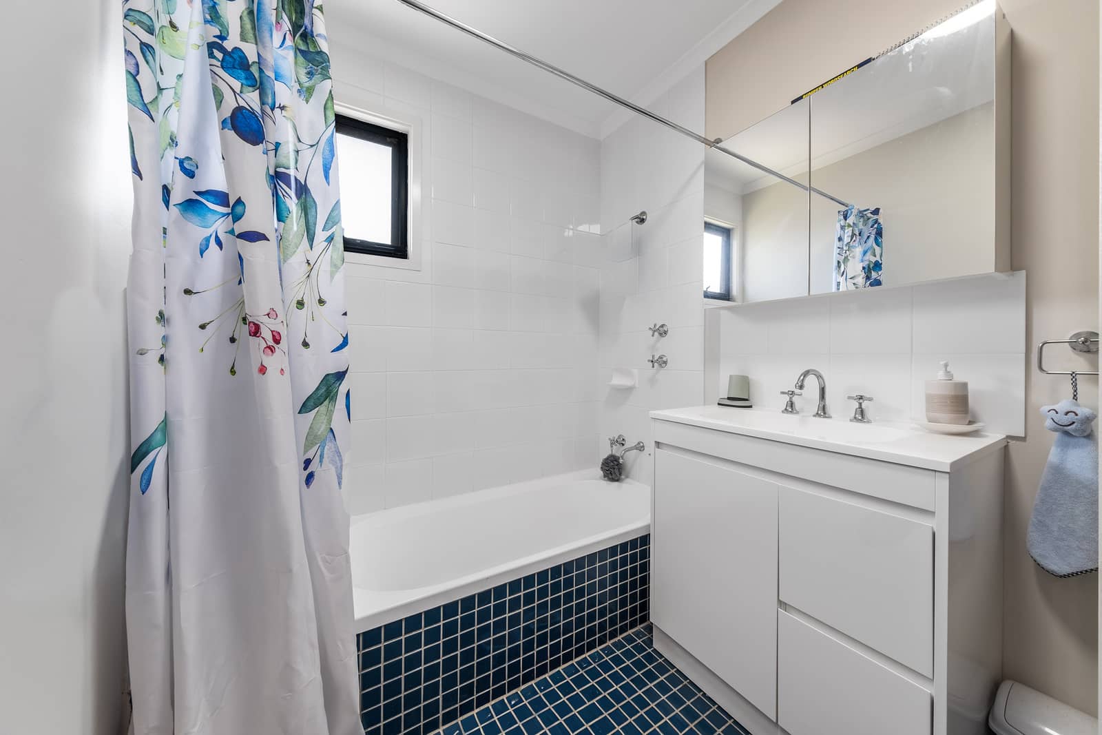 A clean, modern bathroom with a white vanity, bathtub and blue tiled floor.