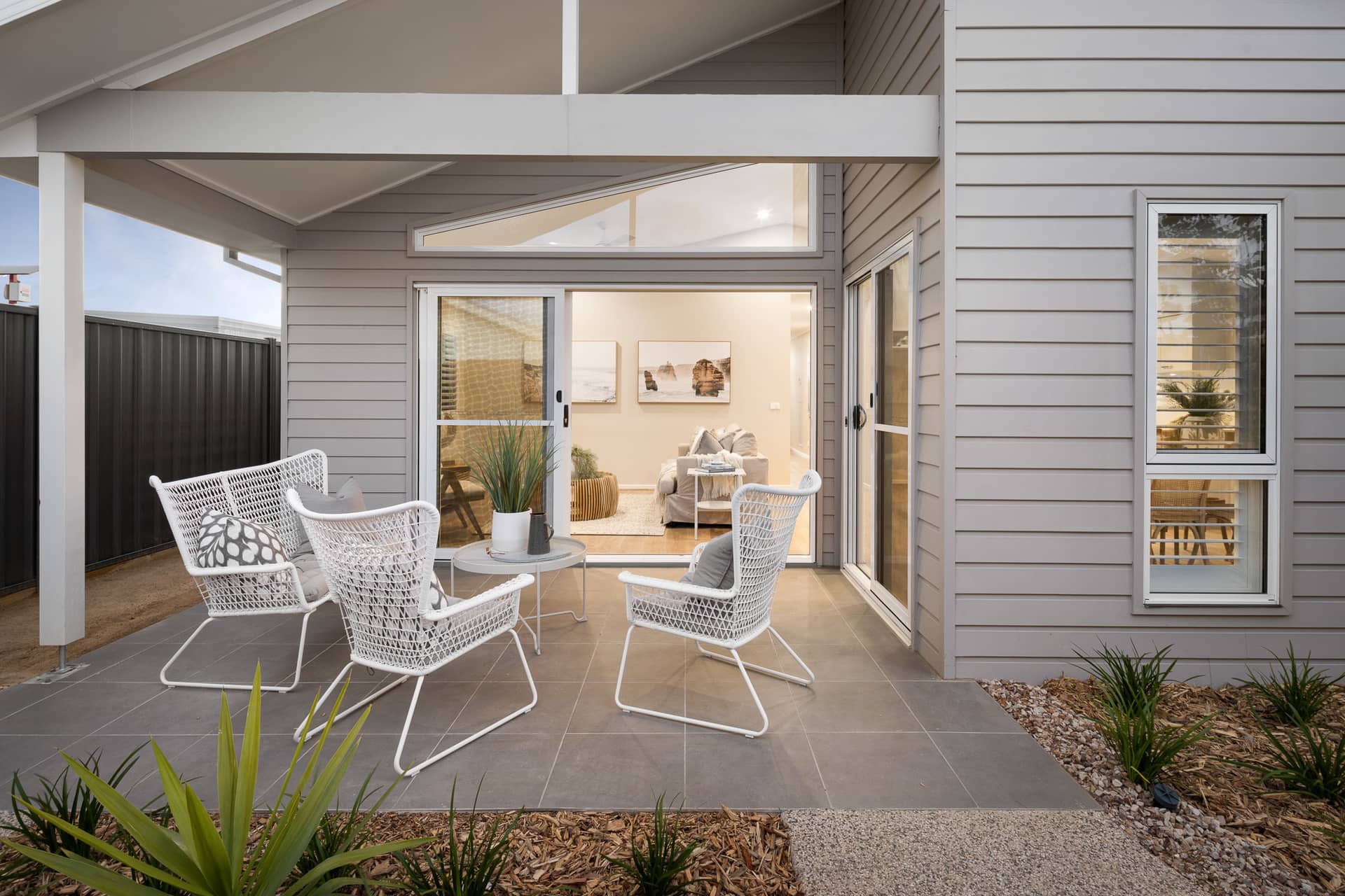 Outdoor patio with white woven chairs and a small table, opening into a living room.