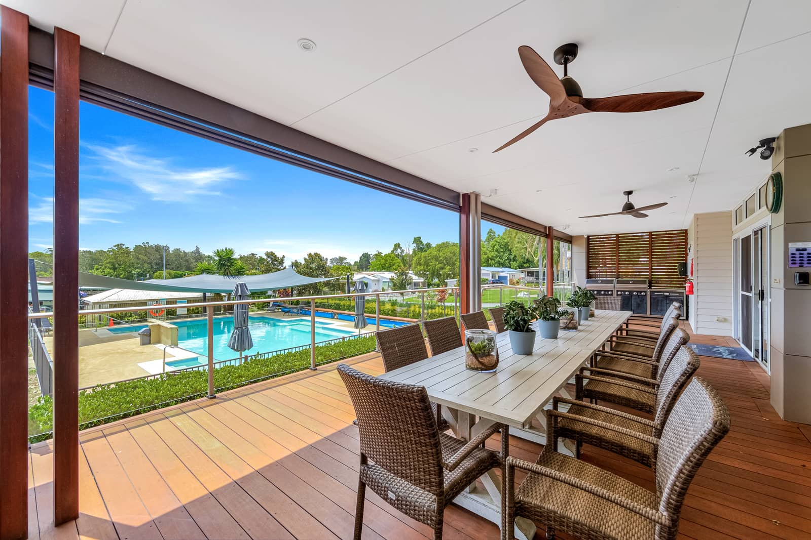 Outdoor dining area with a long table and chairs overlooking an Ingenia Lifestyle community pool.