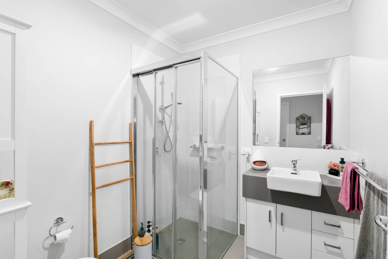 Modern bathroom with a glass-enclosed shower, white vanity, sink, and mirror.