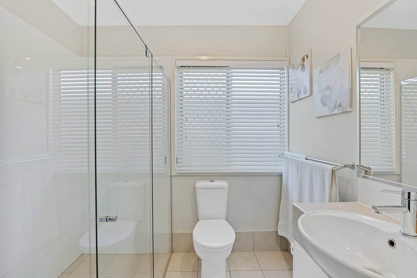 A modern bathroom with a white toilet, sink, and a glass-enclosed shower in an Ingenia Lifestyle community.