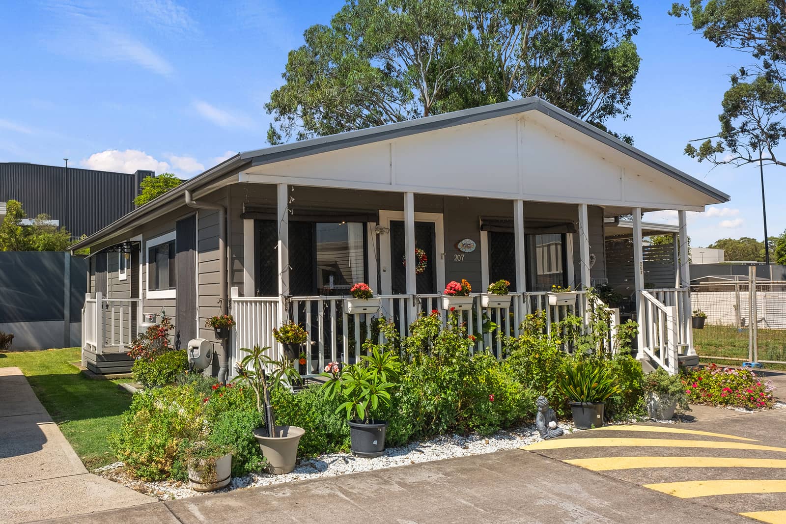 A grey Ingenia Lifestyle land lease home with a white-railed veranda overflowing with plants and flowers.