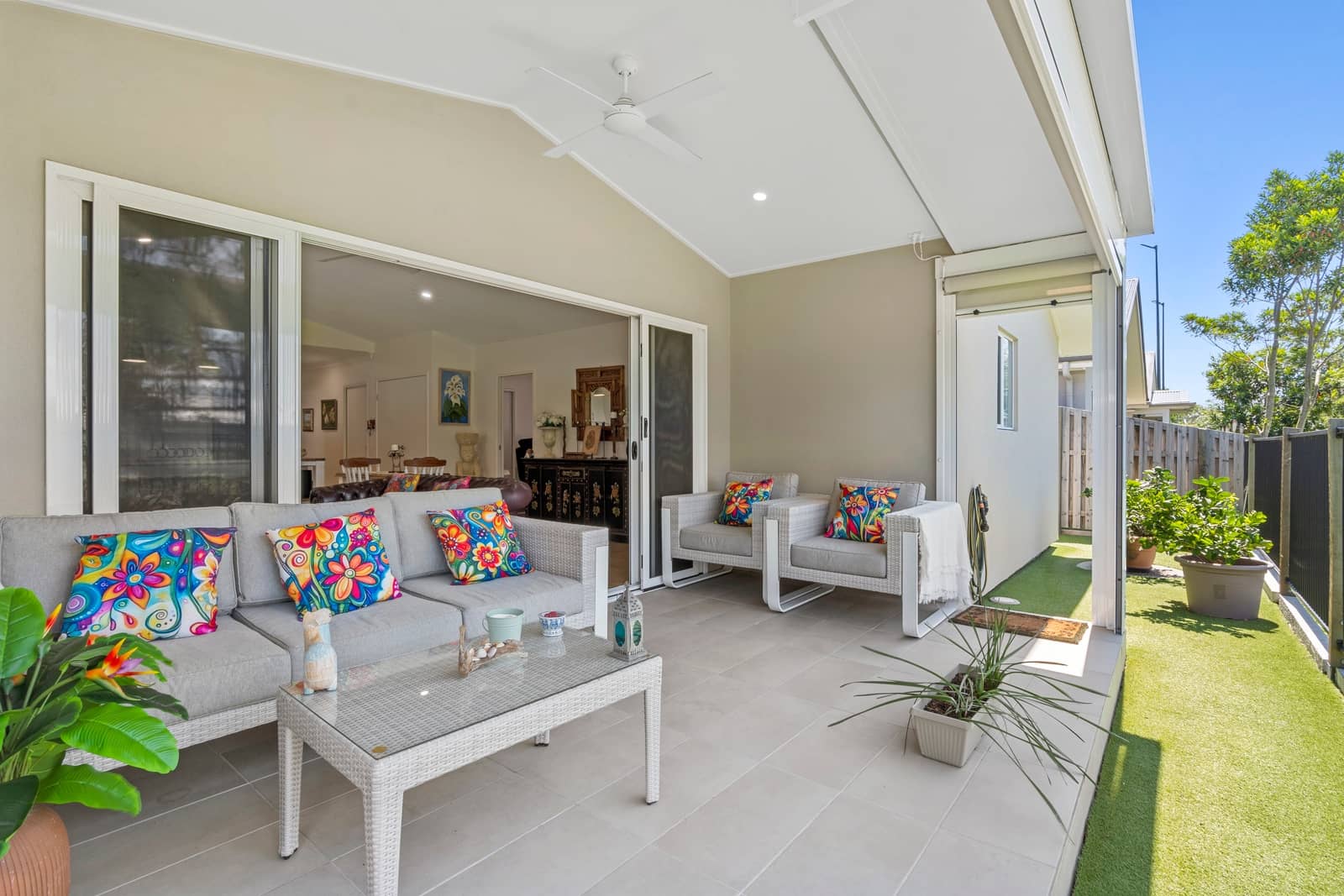 Outdoor patio with a grey sofa and armchairs decorated with colourful cushions, a glass coffee table and artificial turf.